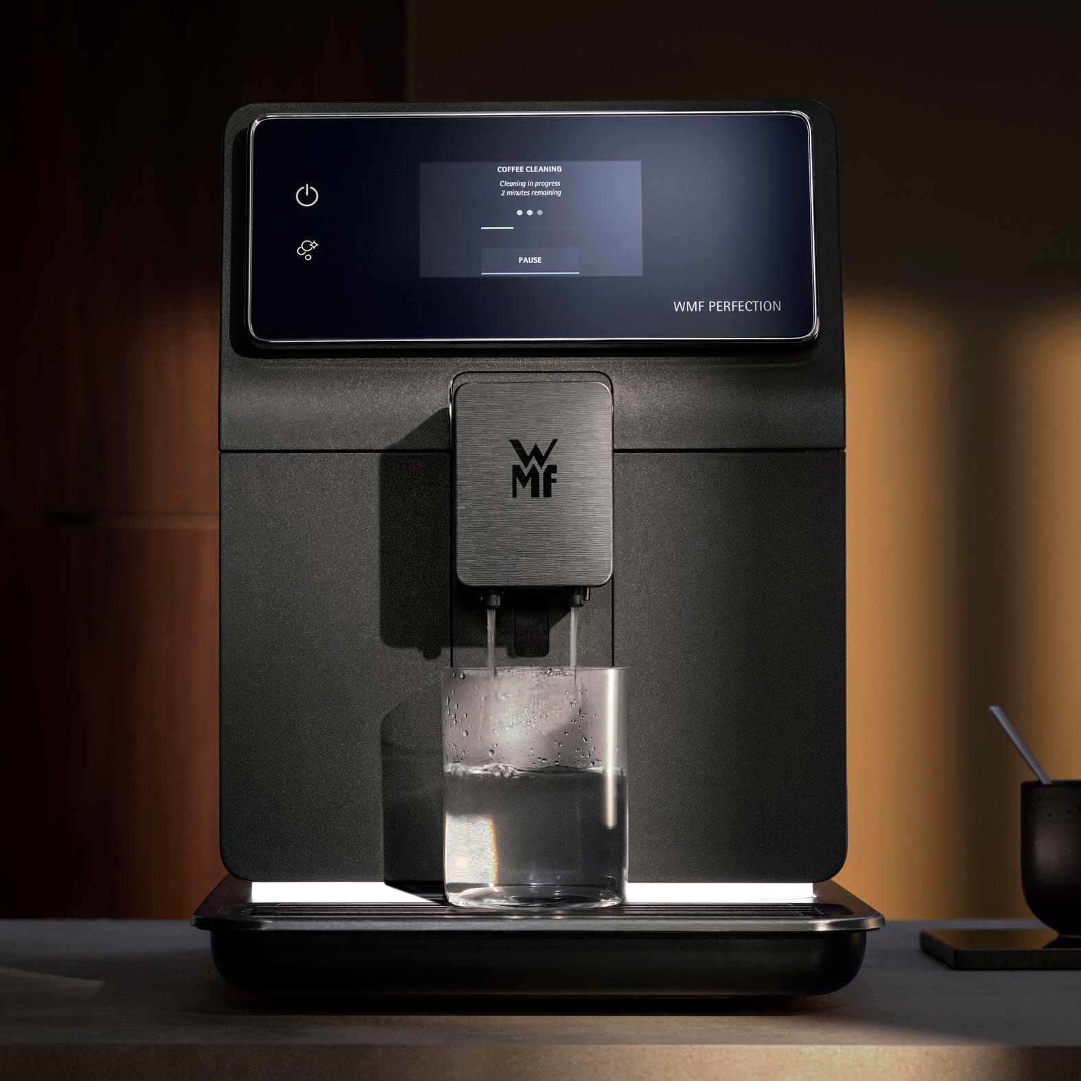 Eine schwarze Kaffeemaschine gibt Wasser in ein Glas ab. Auf dem Bildschirm steht 'Kaffeereinigung' und '2 Minuten verbleibend'.