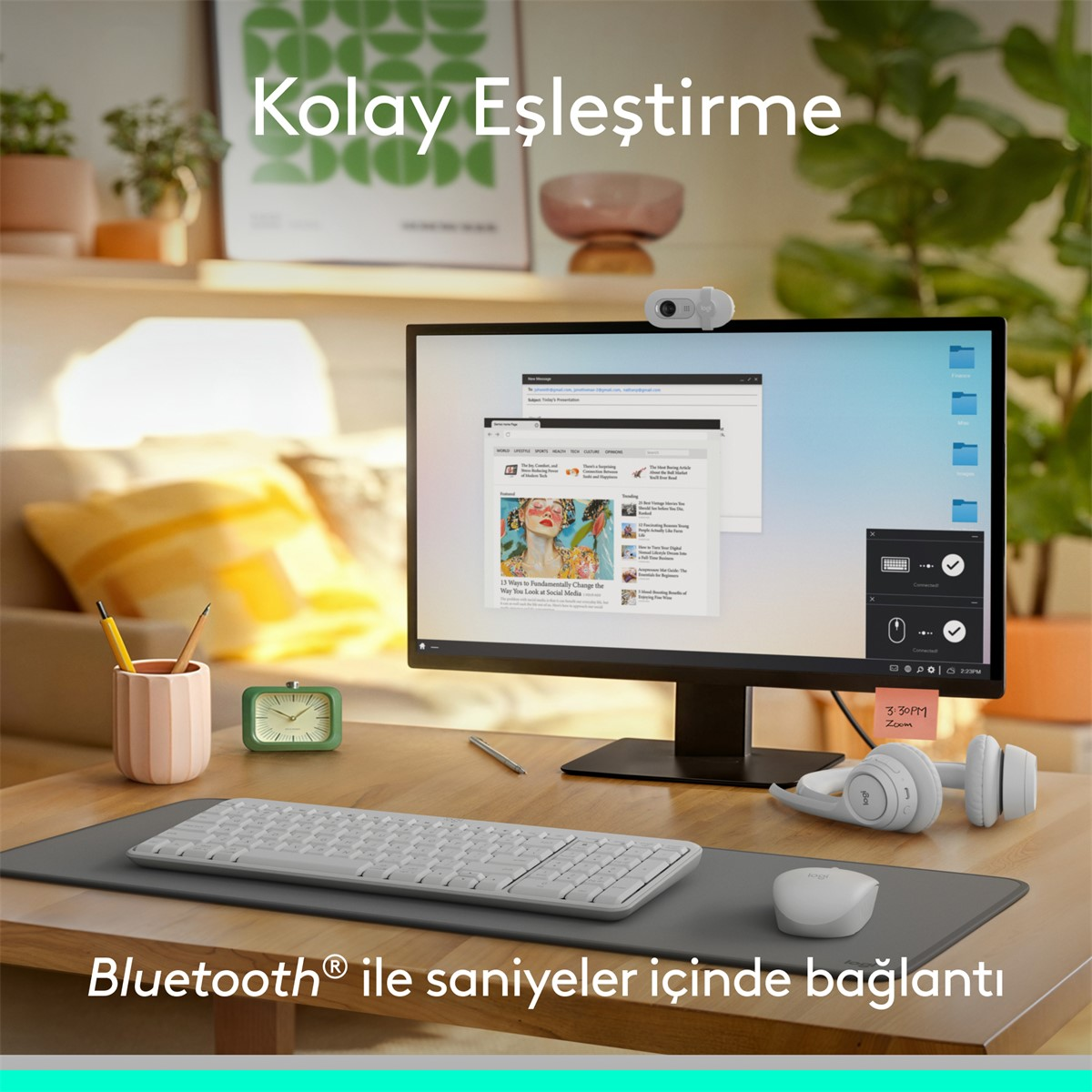 Bir monitör, klavye, fare, web kamerası ve kulaklıklarla bir masa düzeni. Bir saat ve kalemlik de görünür.