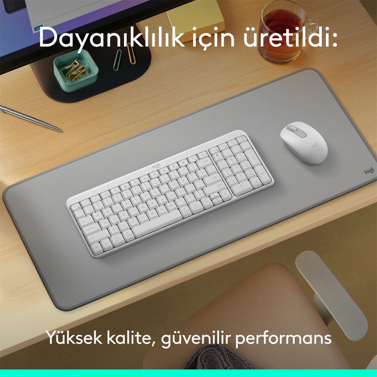 Ahşap bir masada beyaz klavye, fare ve masa pedi. Sağda bir fincan çay var. Metin şöyle diyor: 'Yüksek kalite, güvenilir performans'.