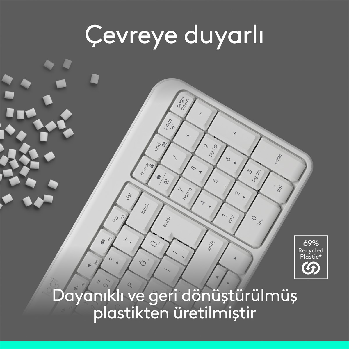 Gri bir yüzey üzerinde siyah tuşlu beyaz bir klavye. Klavyede geri dönüşüm sembolü ve geri dönüştürülmüş plastik hakkında metin var.