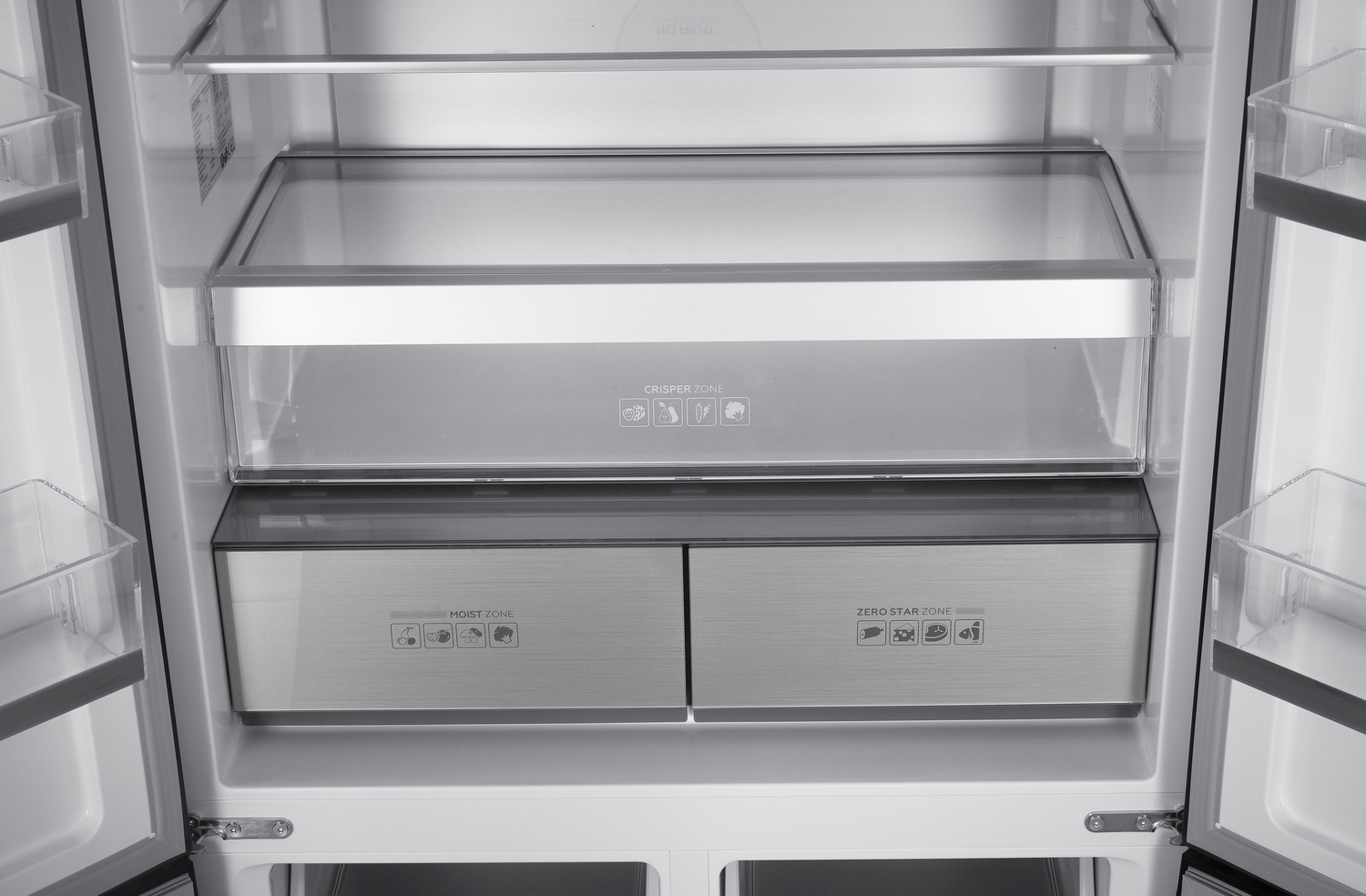 Interior de un refrigerador. Tiene estantes, cajones con la etiqueta 'Crisper Zone', 'Moist Zone' y 'Zero Star Zone'. Colores blanco y metálico.