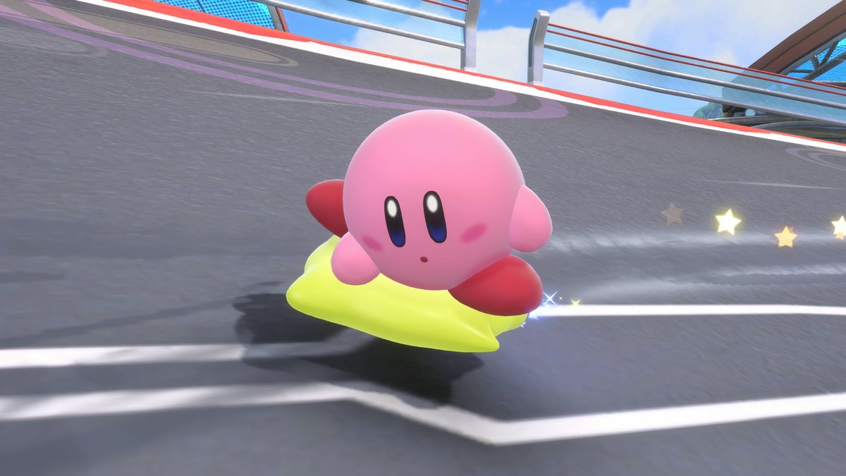 Pink Kirby on a yellow cushion floats on a race track. Stars trail behind him, suggesting speed and motion.