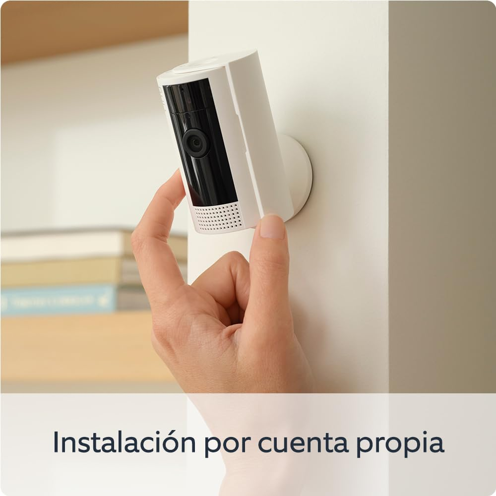 Una mano sujeta una cámara de seguridad blanca en una pared blanca. Texto que pone: instalación por cuenta propia.