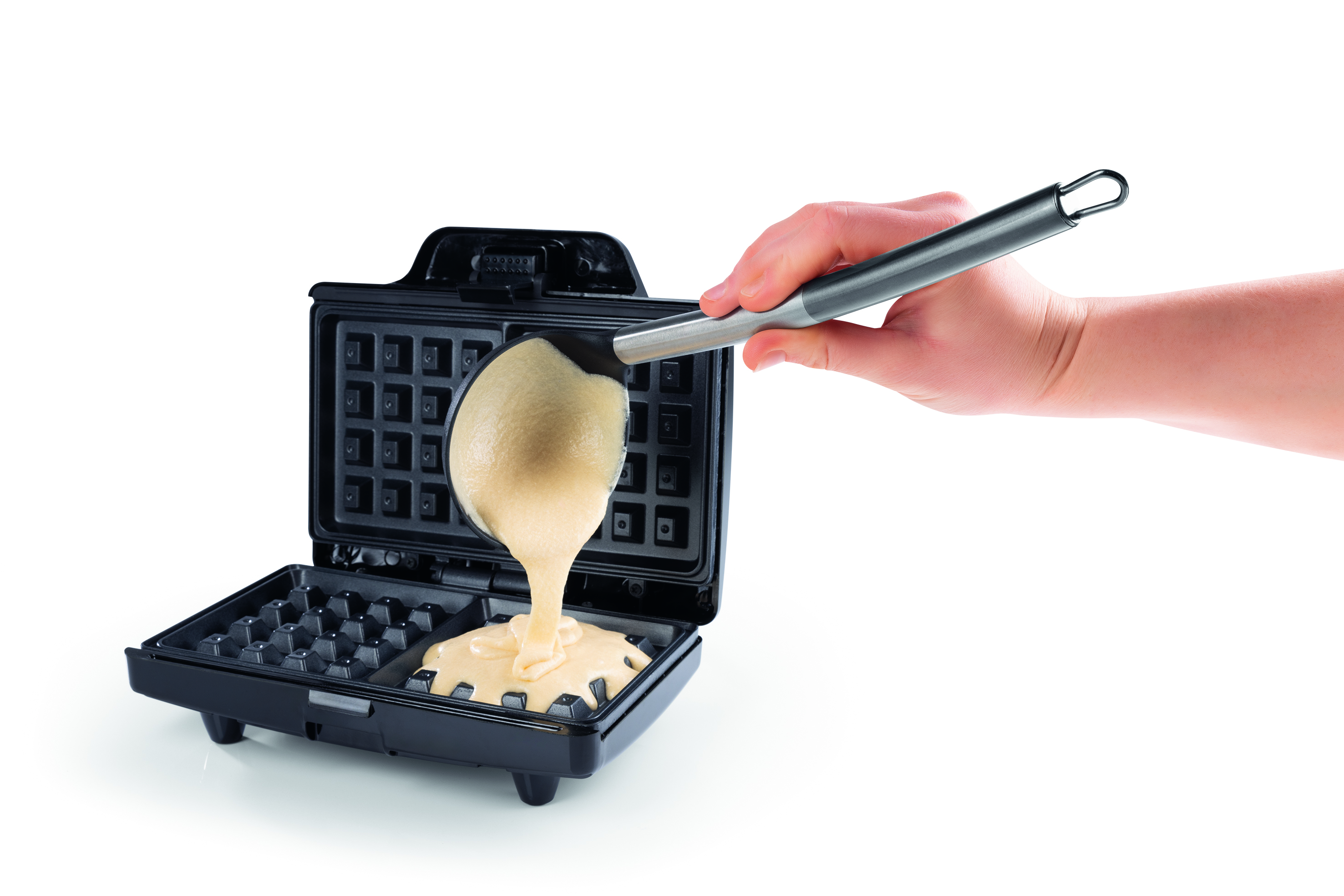 Eine Hand gießt Teig mit einer Kelle in ein offenes, schwarzes Waffeleisen auf weißem Untergrund.