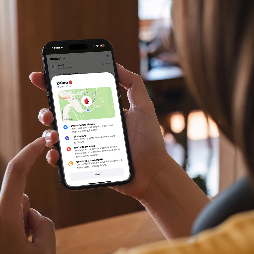 Eine Person hält ein Telefon, das eine Karte mit dem Standort eines Rucksacks anzeigt. Der Bildschirm zeigt Optionen zum Auffinden des Gegenstands an.