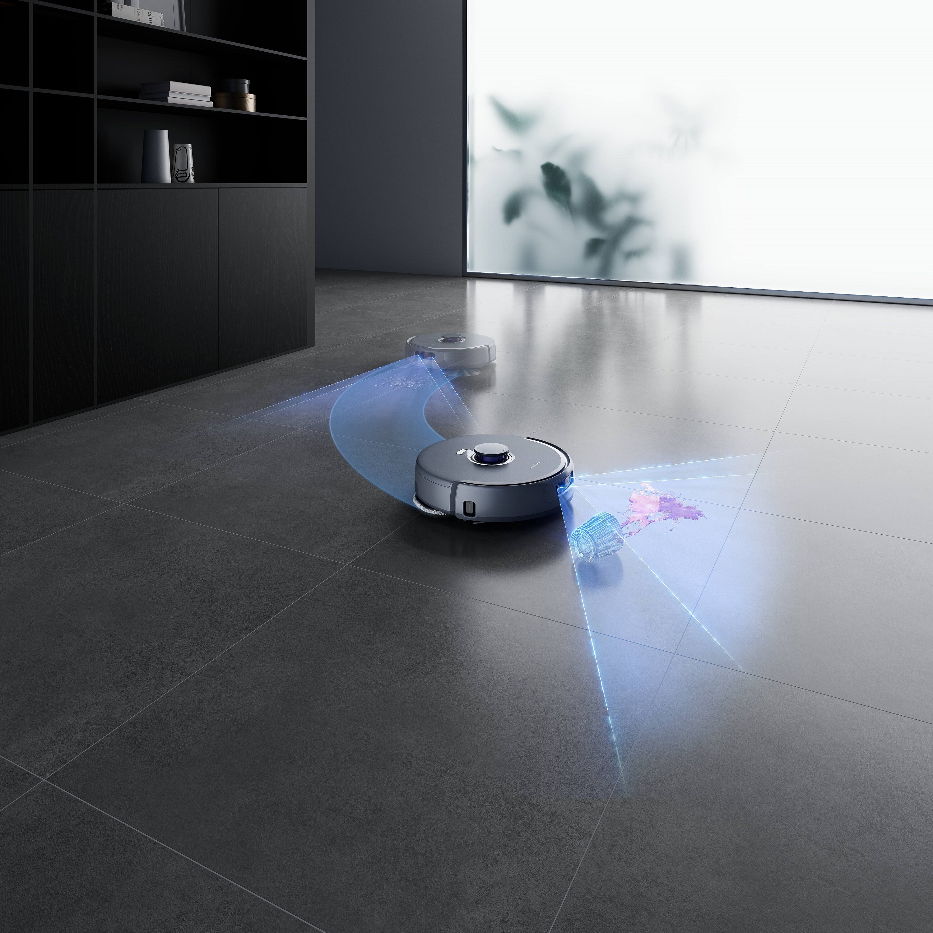 Dwa roboty sprzątające na kafelkach, jeden czyści rozlaną ciecz. Czarna szafka i ściana ze szkła mrożonego w tle.