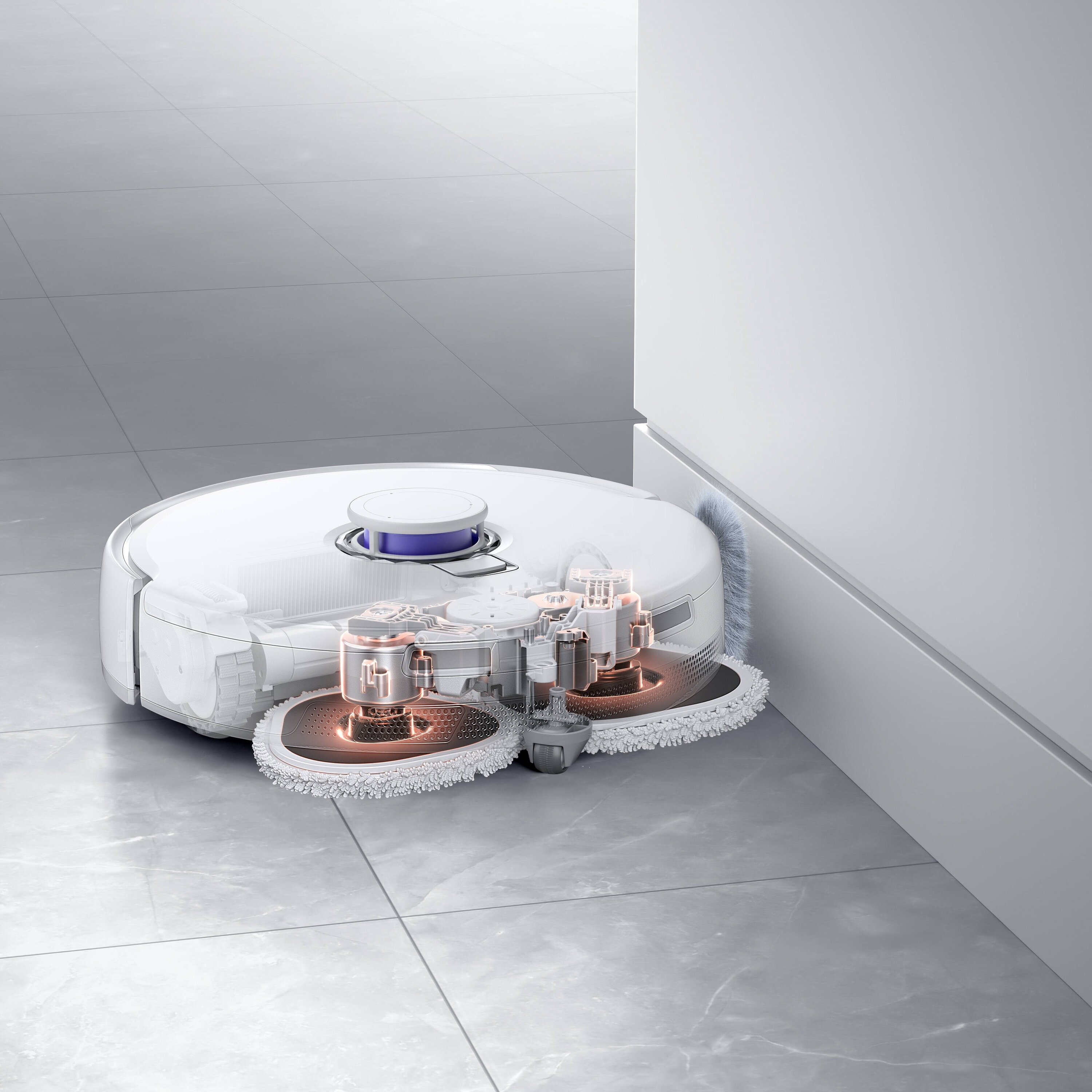 Biały robot sprzątający na szarej podłodze z płytek. Znajduje się blisko białej ściany.