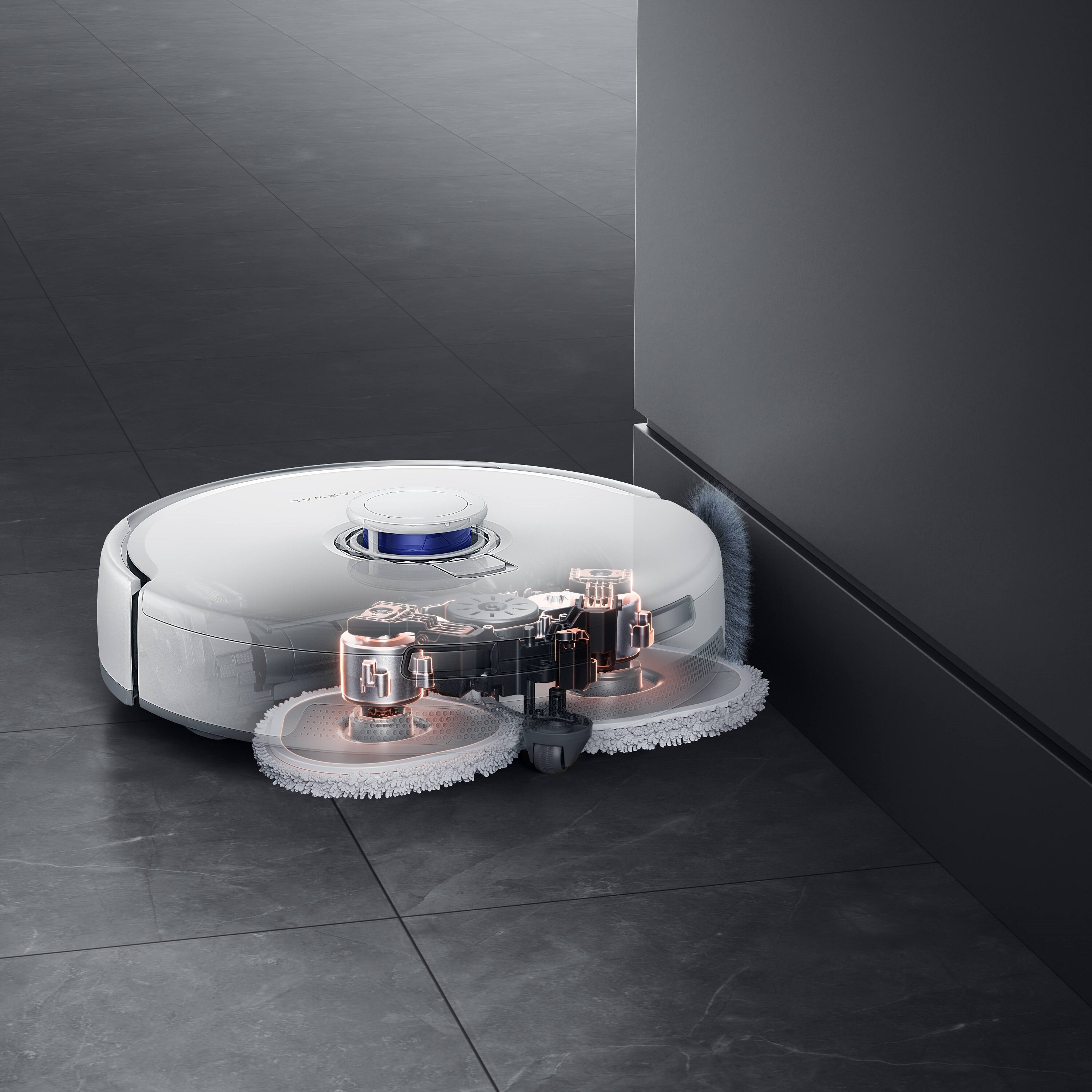 Biały robot odkurzający na szarej podłodze z płytek. Maszyna stoi obok ciemnoszarej ściany.