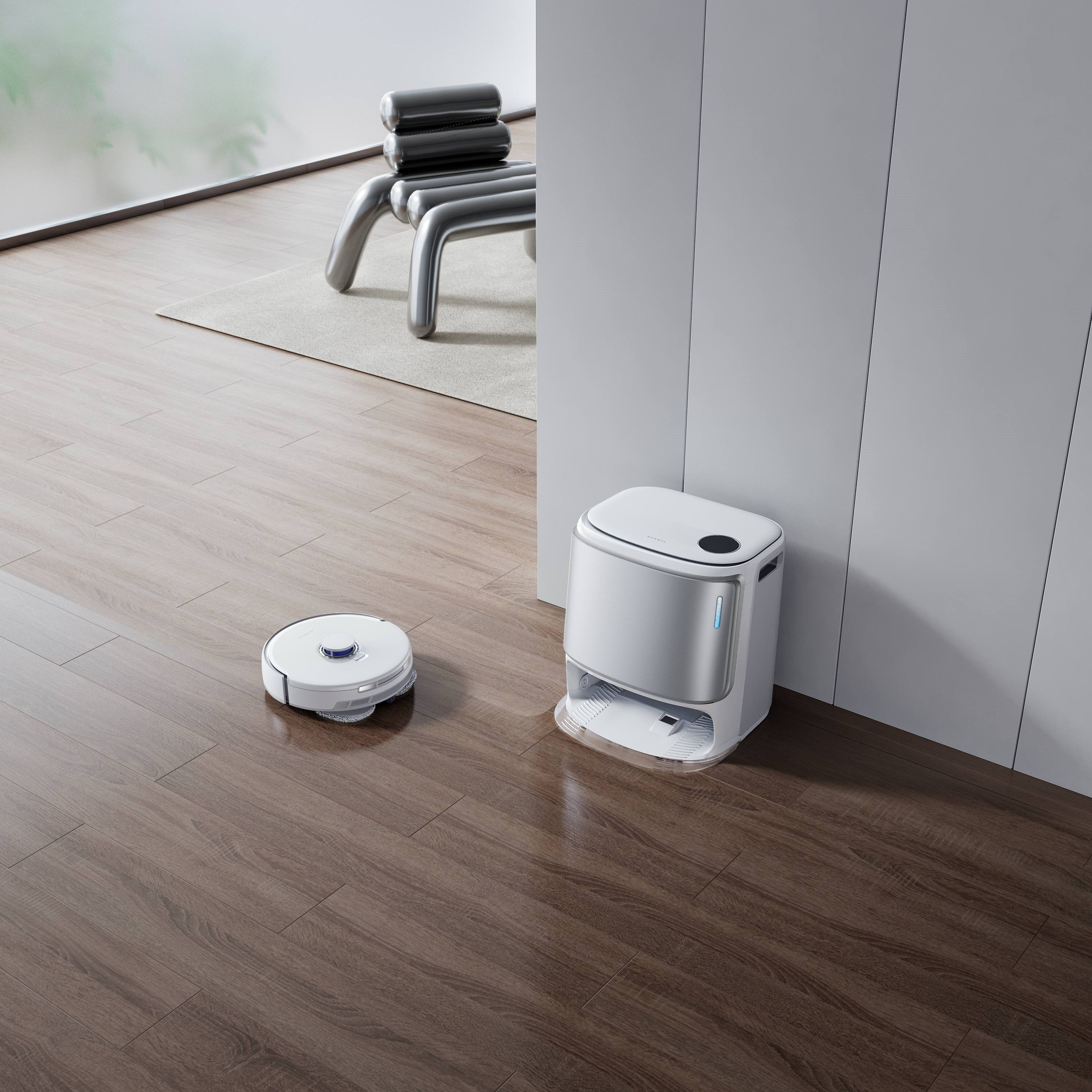 Robot odkurzający i stacja ładująca na drewnianej podłodze. Metalowe krzesło w tle.