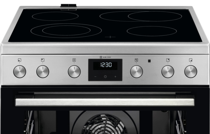 Nowoczesny piekarnik ze stali nierdzewnej z czarną szklaną płytą grzewczą z czterema okrągłymi palnikami. Drzwi piekarnika są otwarte.