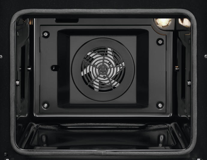 Wnętrze czarnego piekarnika, wentylator jest wyśrodkowany. Wokół metalowe części i światło u góry po prawej.
