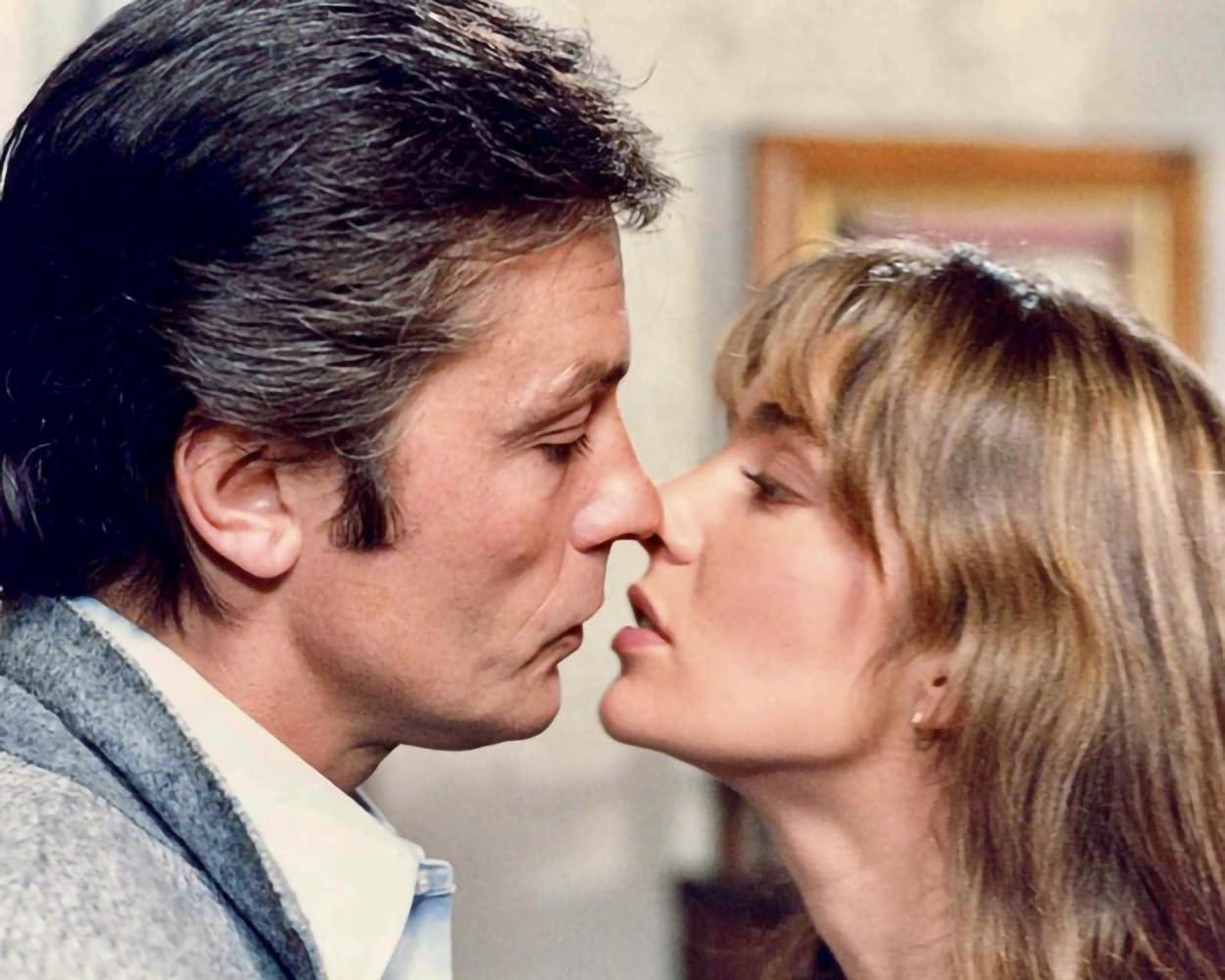 Ein Mann und eine Frau kurz vor dem Küssen. Der Mann hat dunkles Haar. Die Frau hat blondes Haar. Im Hintergrund hängt ein Gemälde.