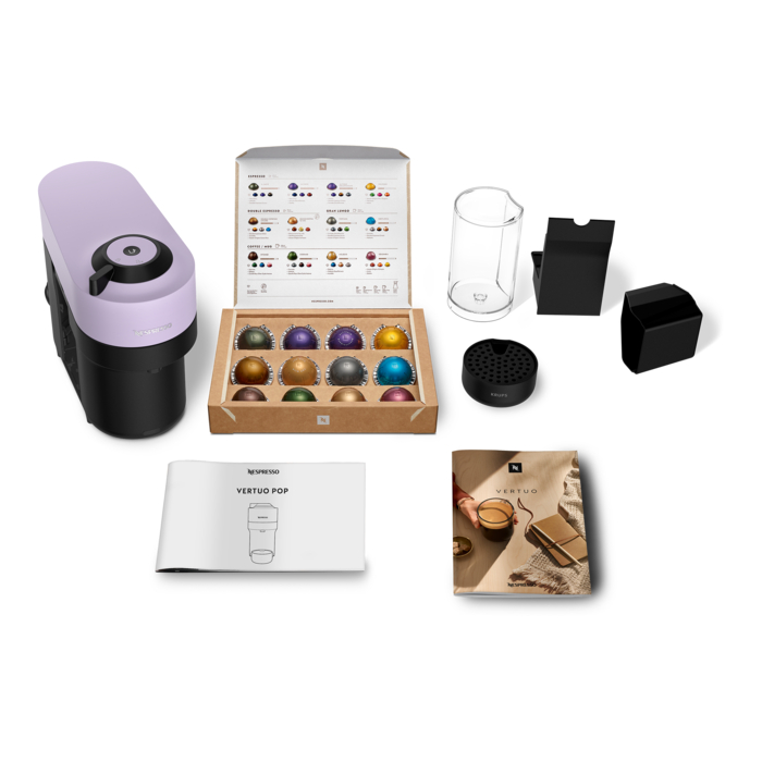 Eine Nespresso Vertuo Pop Kaffeemaschine und Zubehör, darunter Kapseln, Broschüre und Glas, auf einer weißen Oberfläche.