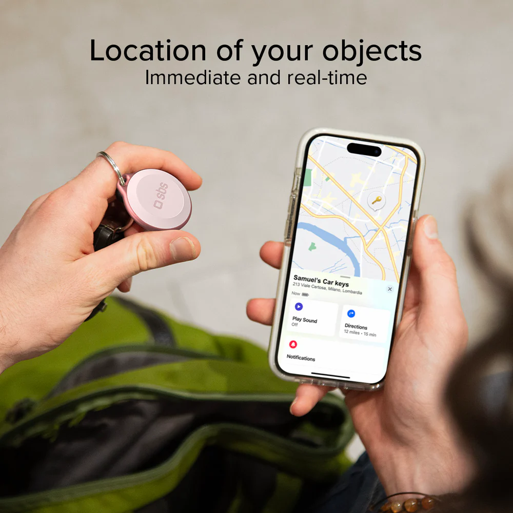 Eine Person hält einen rosafarbenen Tracker und ein Telefon mit einer Karte. Das Telefon zeigt den Standort von Autoschlüsseln.