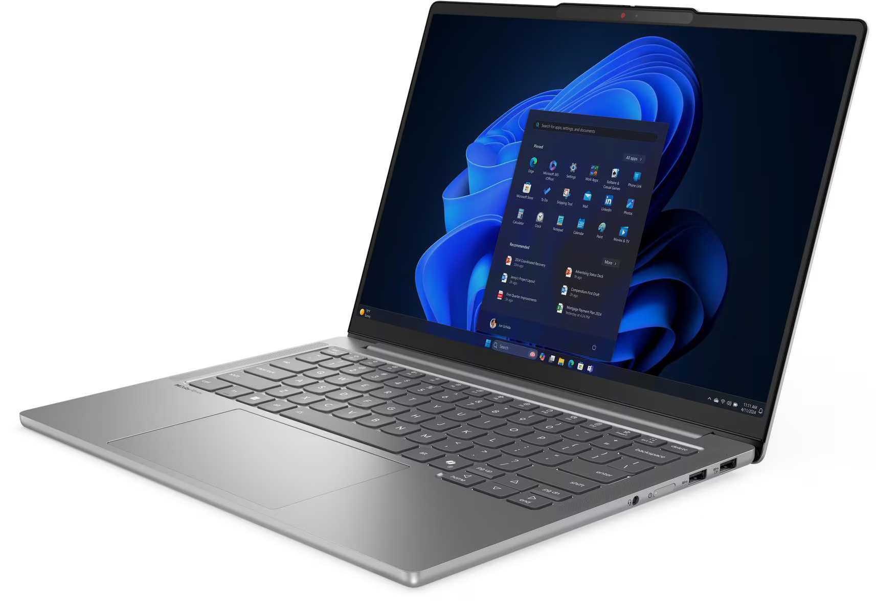 Egy ezüst laptop nyitva van, a Windows 11 felületét mutatja. A képernyőn alkalmazásikonok és a Windows logó látható.