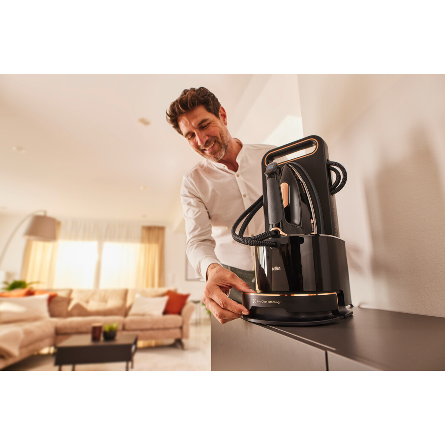A man in a white shirt uses a black iron. The iron is on a black stand, with a gold accent.
