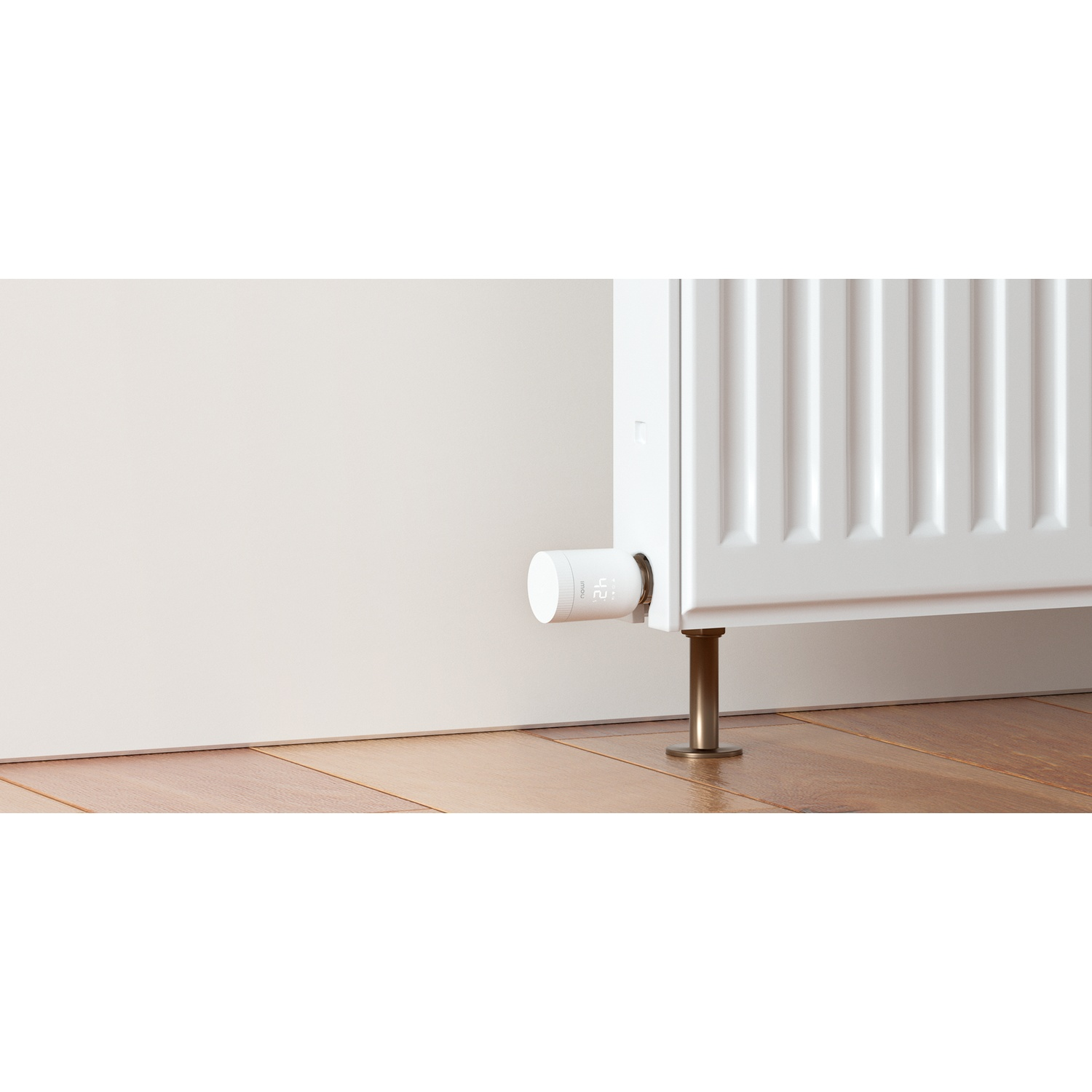 Een witte radiator met een digitale thermostaat. De thermostaat is cilindrisch en bevestigd aan de radiator. Houten vloer zichtbaar.
