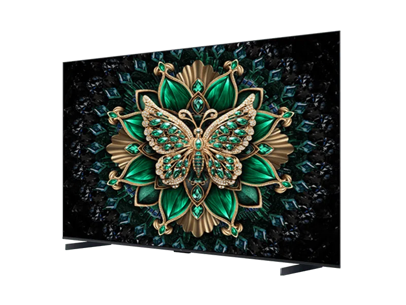 Egy TV egy ékszerrel díszített pillangót jelenít meg egy arany és zöld virágszerű mintán. A háttér sötét, geometrikus formákkal.