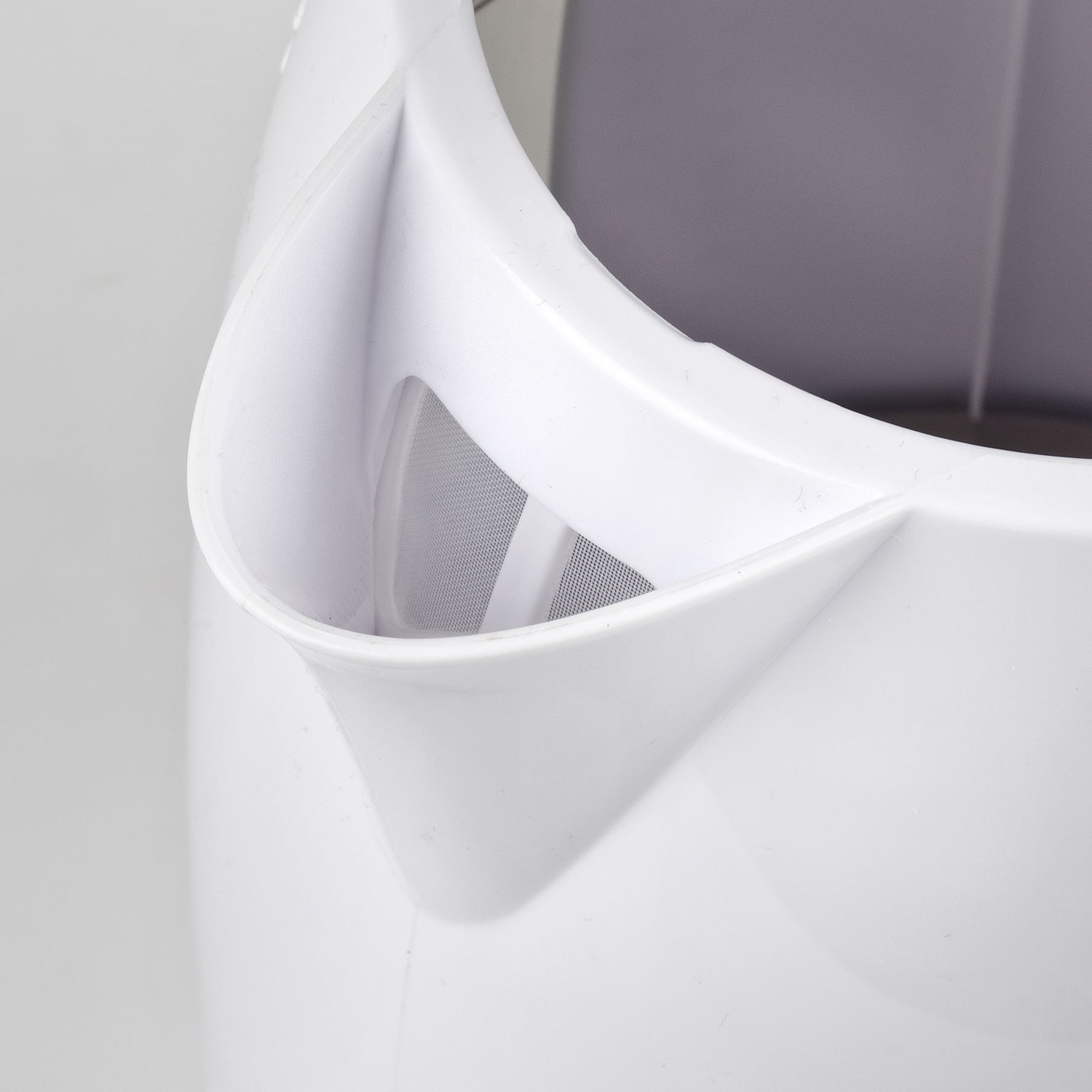 Primo piano di un beccuccio di un bollitore elettrico bianco. All'interno è visibile un filtro a rete. Lo sfondo è grigio chiaro.