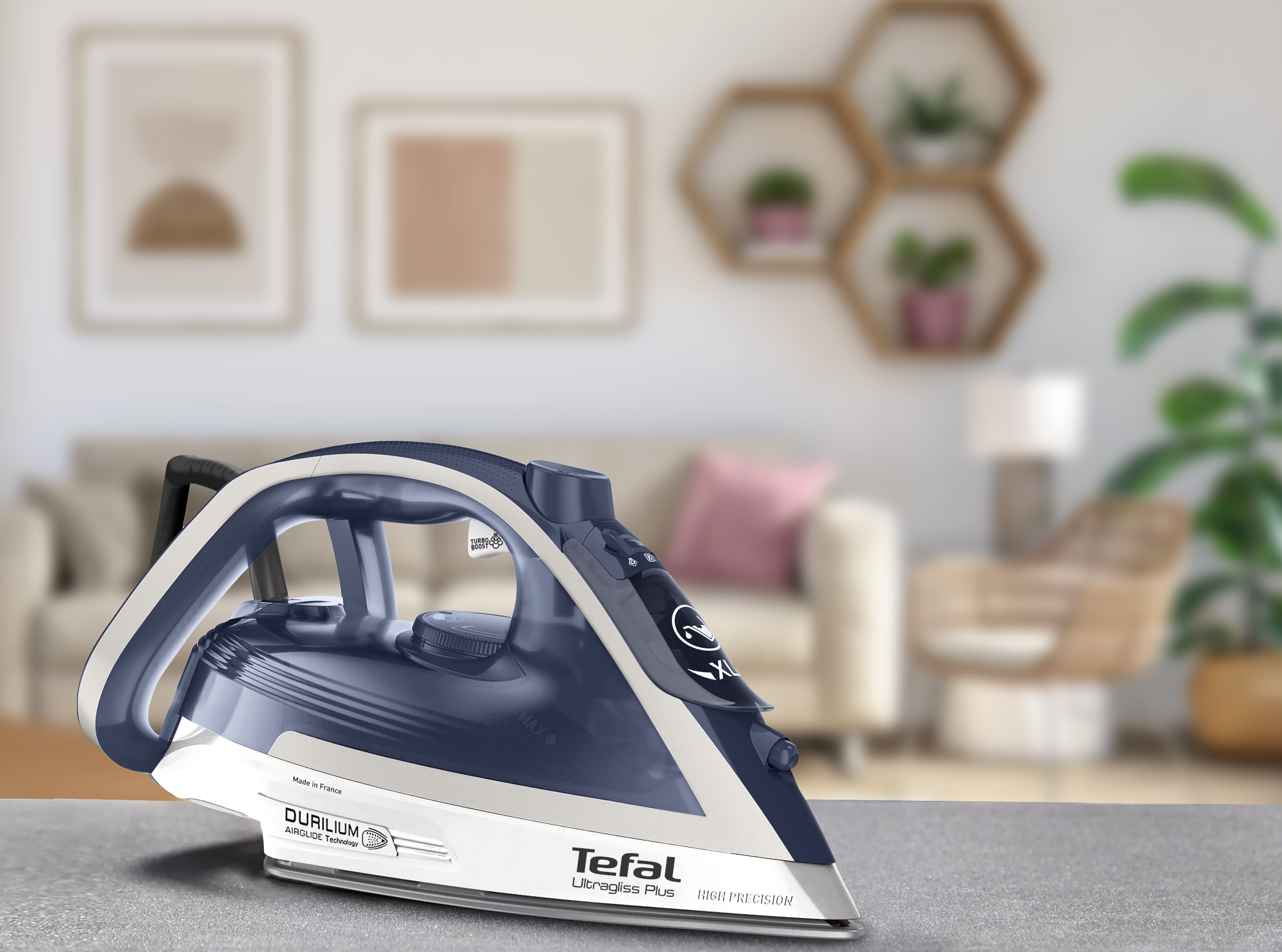 Egy Tefal vasaló az asztalon, elmosódott nappali háttérrel. A vasaló kék és fehér.