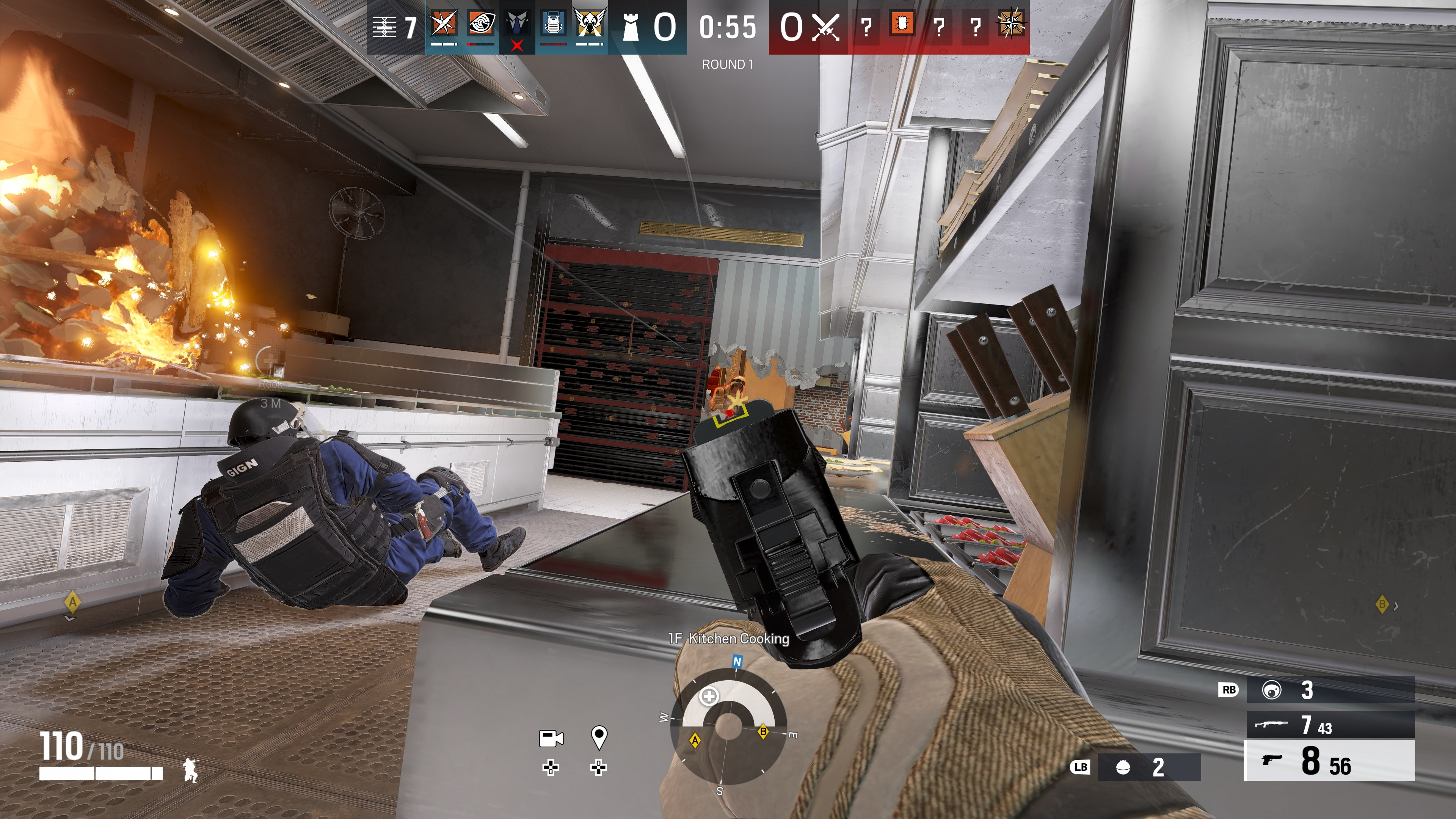 Ego-Perspektive eines Shooter-Spiels. Ein Spieler zielt mit einer Waffe in einer Küche, Explosion und gefallener Spieler sichtbar.