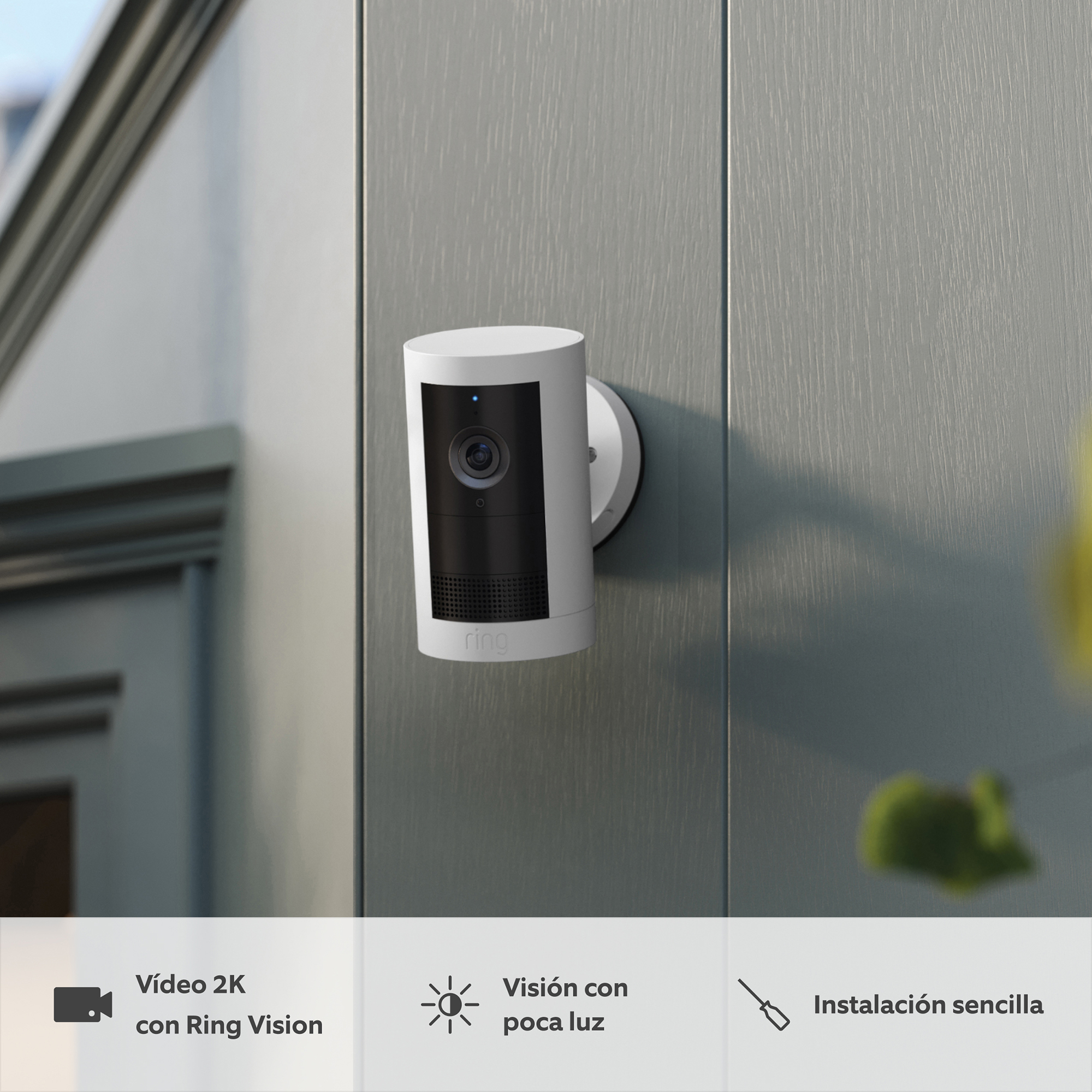 Una cámara de seguridad Ring blanca montada en una pared de madera gris. Tiene una parte delantera negra y una luz azul.
