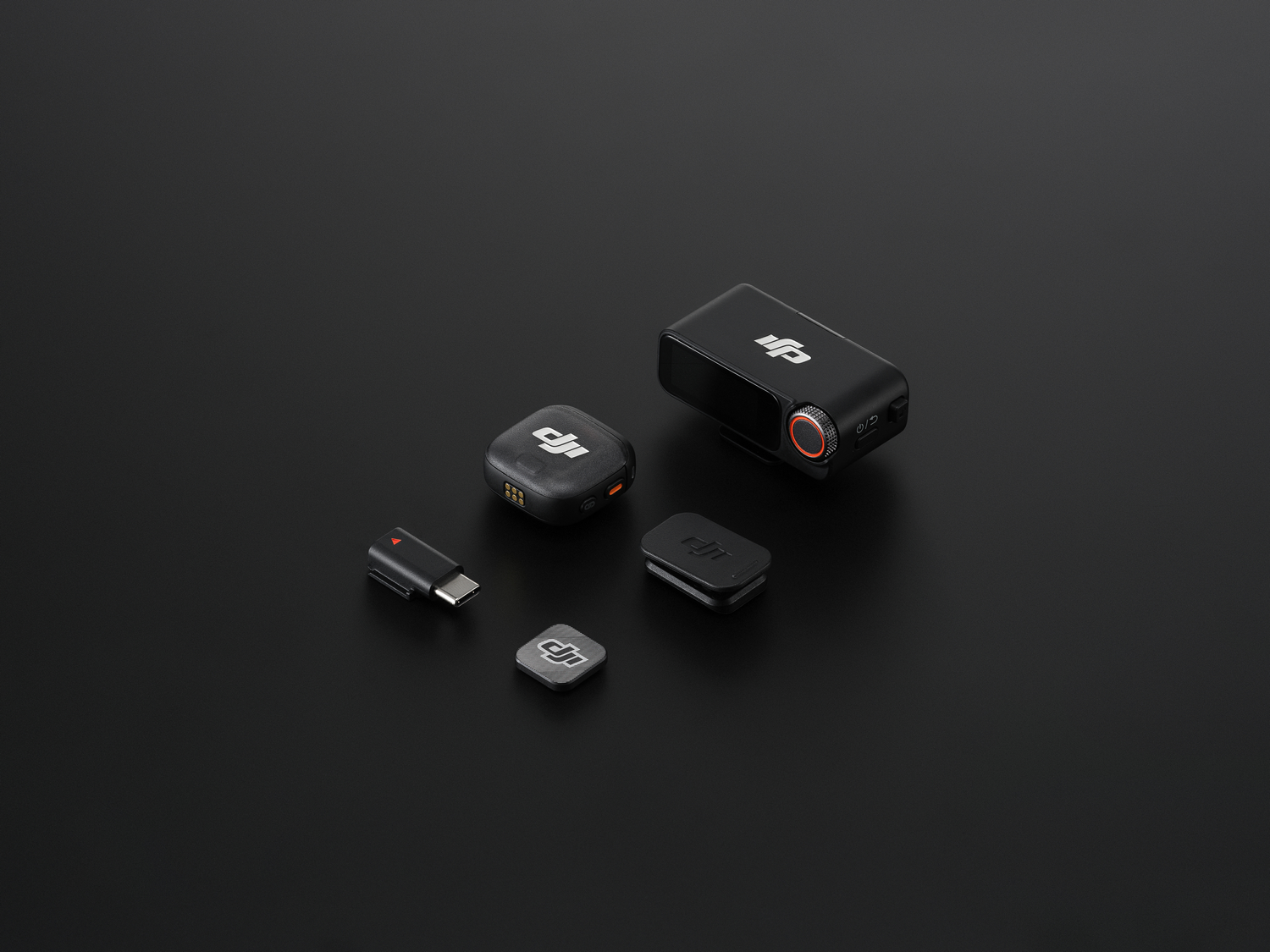Gadgets tecnológicos negros sobre una superficie negra. Incluye receptor, transmisor, adaptador y accesorios. Logotipo DJI visible.