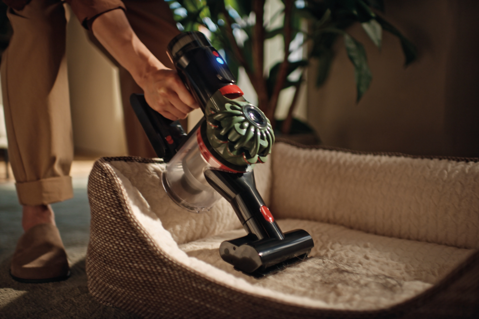 Osoba odkurza legowisko dla psa czarno-srebrnym odkurzaczem. Legowisko jest jasnobrązowe i ma miękki materiał w środku.