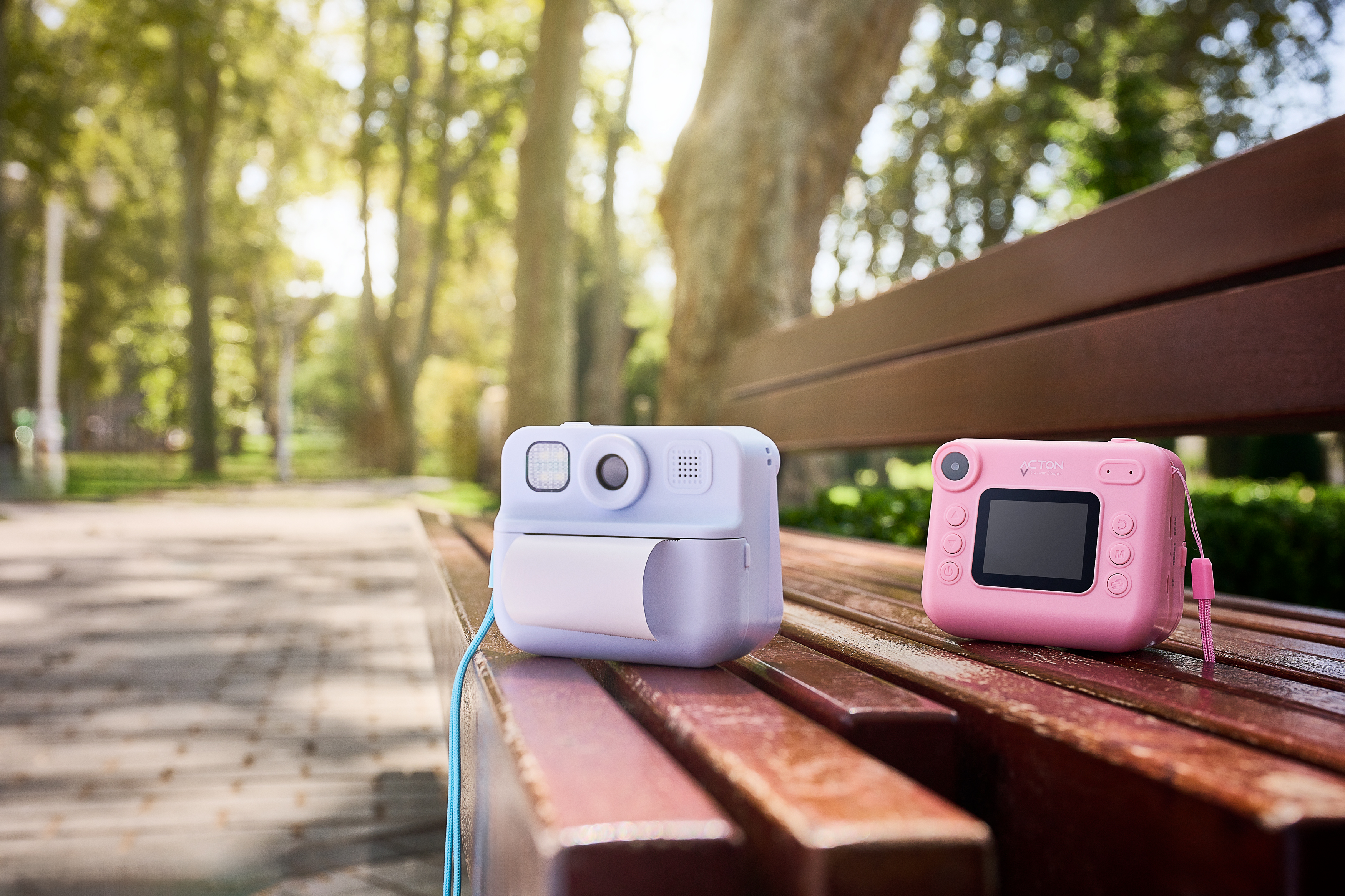 Bir parkta bir bankta iki anında fotoğraf makinesi. Biri lavanta rengi, diğeri pembe.