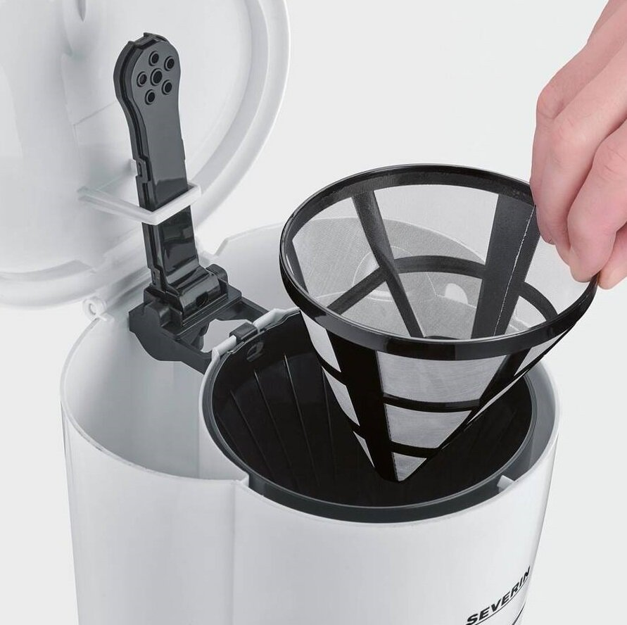 Ręka wkłada filtr do kawy do białego ekspresu do kawy. Filtr jest czarny. Ekspres do kawy jest biały.