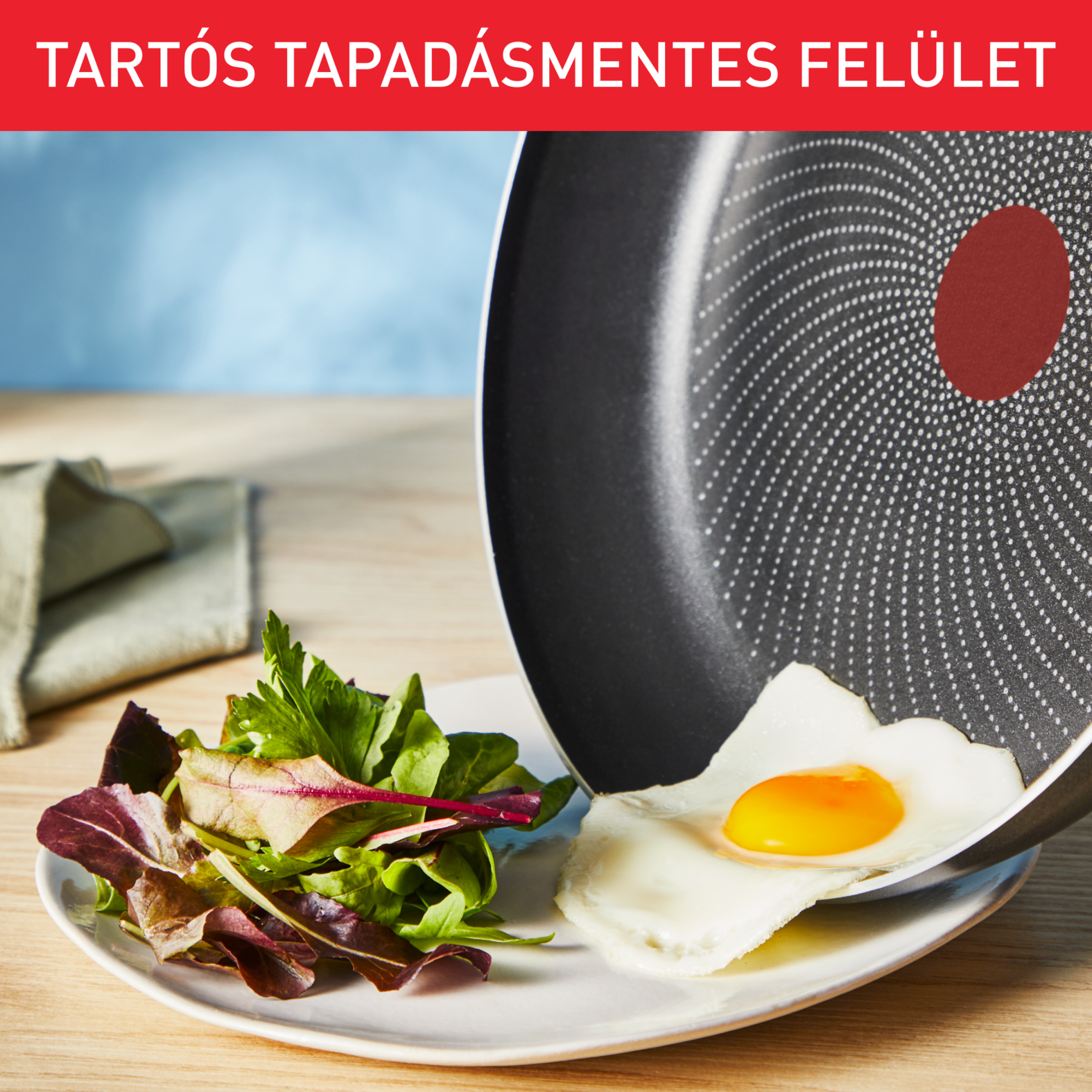 Egy serpenyő tükörtojással és salátával a tányéron. A serpenyőn piros folt van. A háttér elmosódott.
