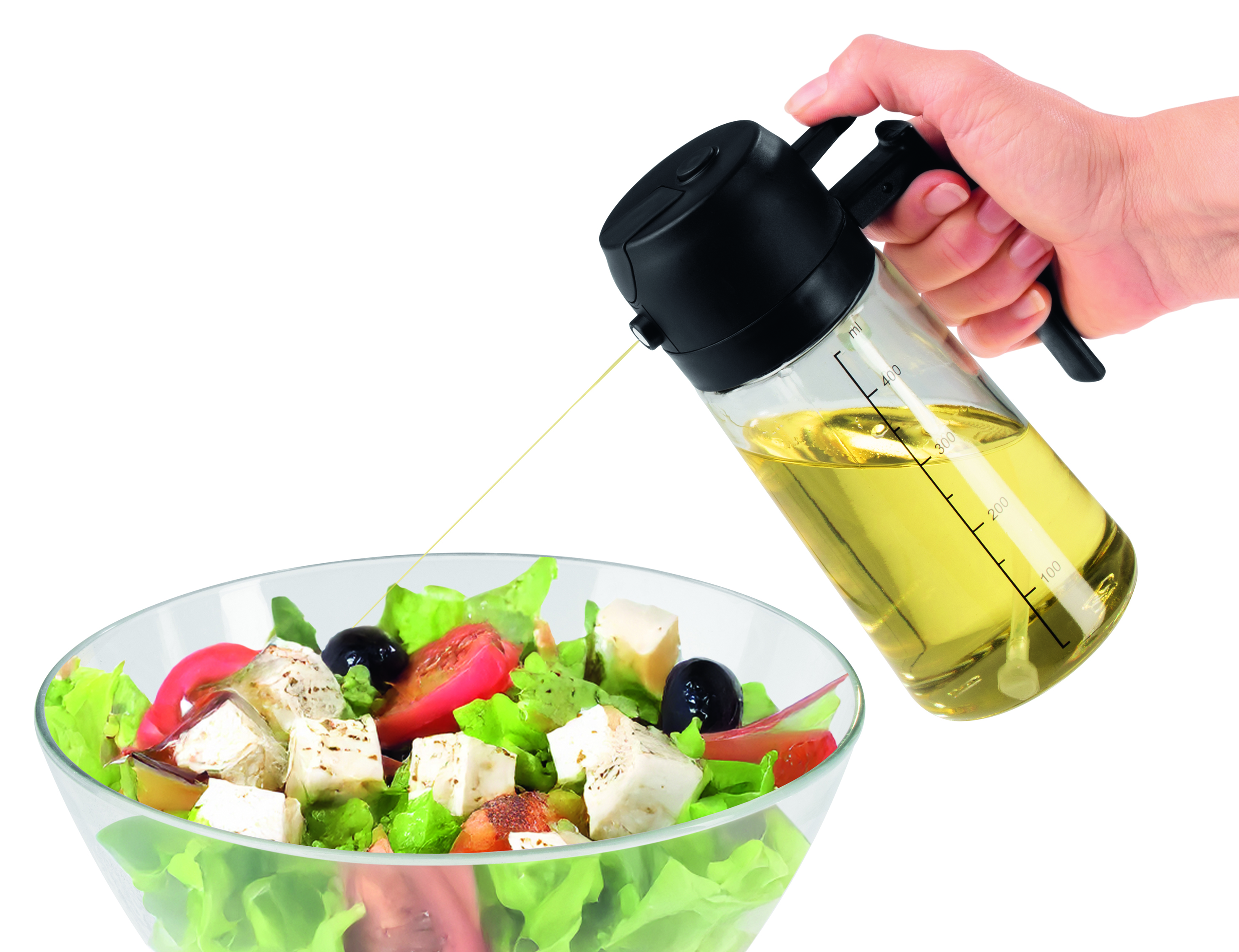 Eine Hand gießt Öl aus einem schwarzen und gläsernen Behälter auf einen Salat. Der Salat enthält Tomaten, Oliven und Käse.