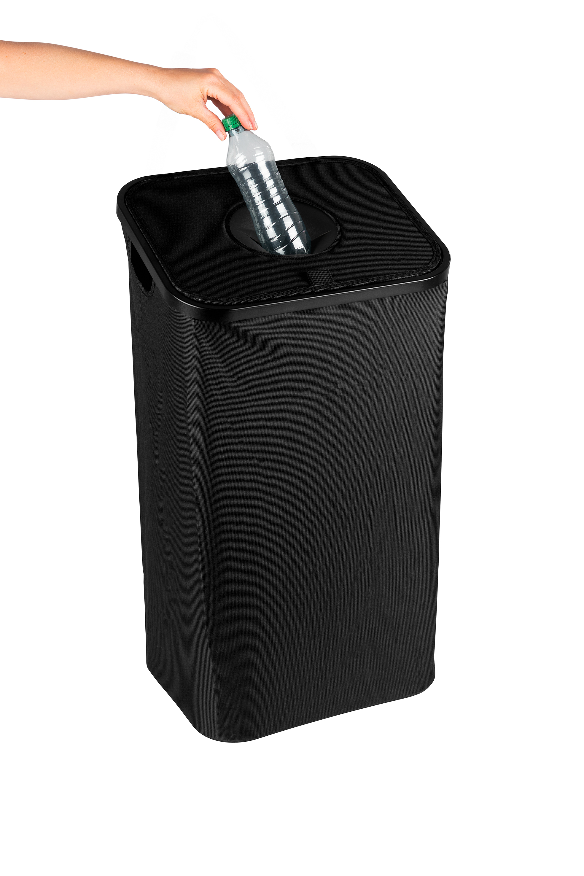 Eine Hand wirft eine Plastikwasserflasche in einen schwarzen Recyclingbehälter. Der Behälter ist hoch und rechteckig.