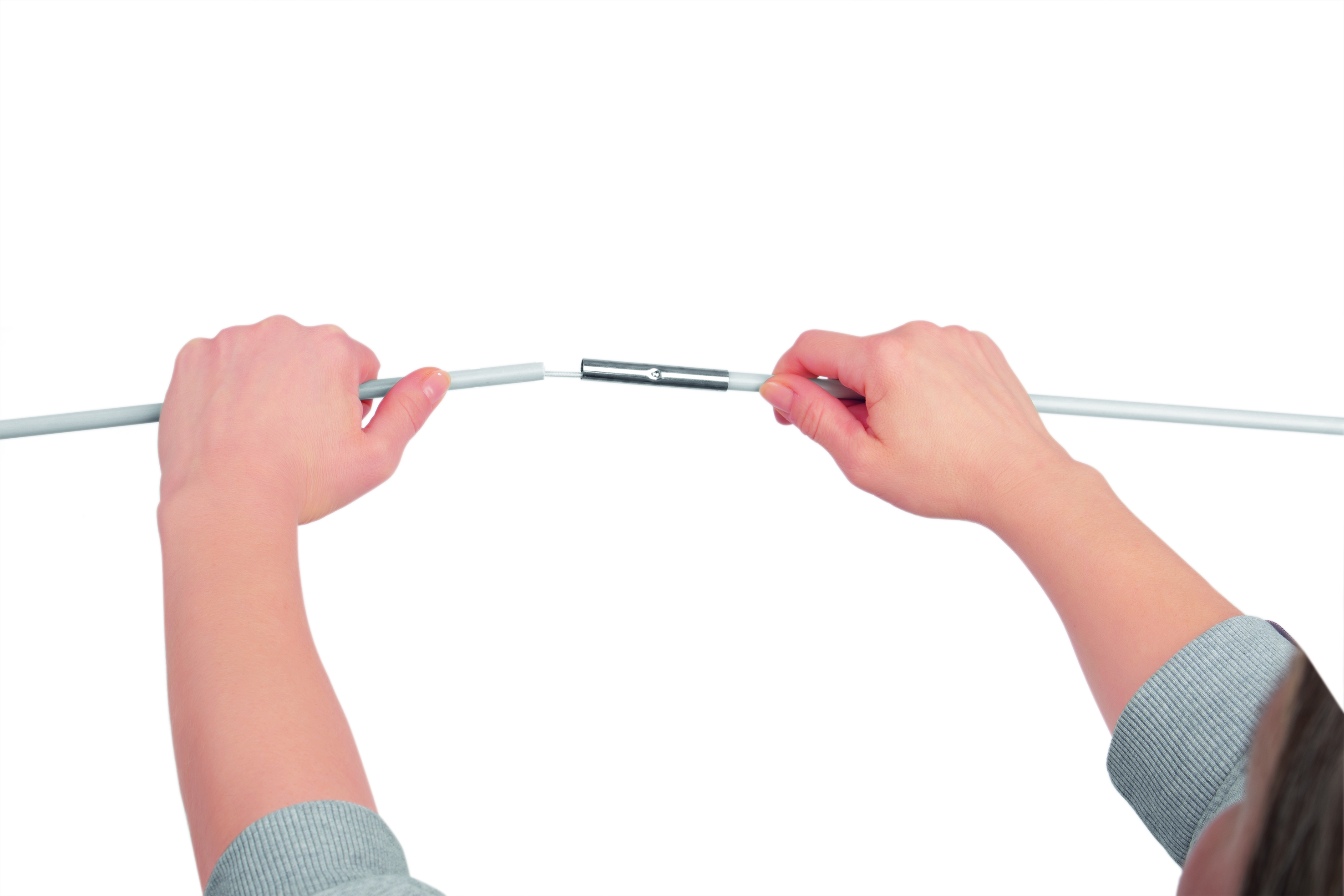 Hände halten ein graues Kabel und verbinden ein Metallteil vor weißem Hintergrund, mit einem grauen Pullover in der Ecke.