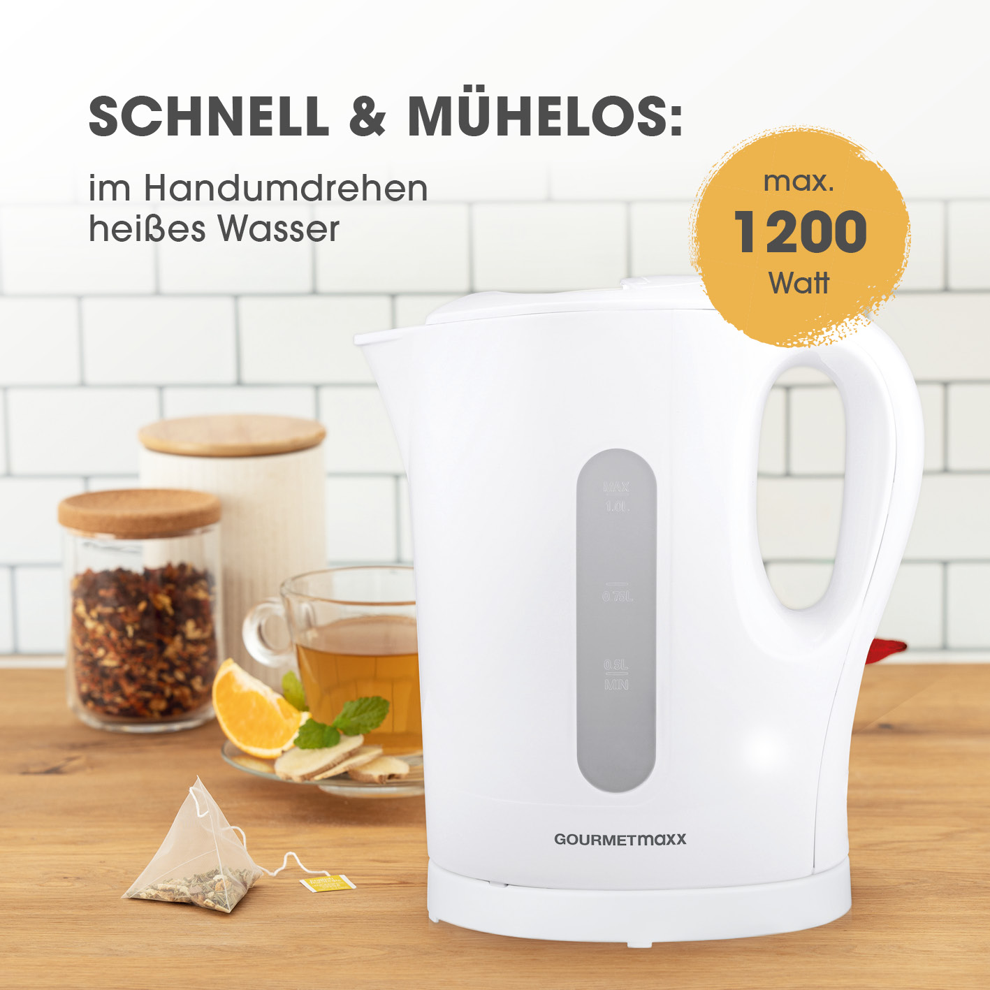 Ein weißer Wasserkocher mit klarer Wasserstandsanzeige. Ein Glas Tee mit Zitrone und Ingwer, Teebeutel und Gläser sind sichtbar.