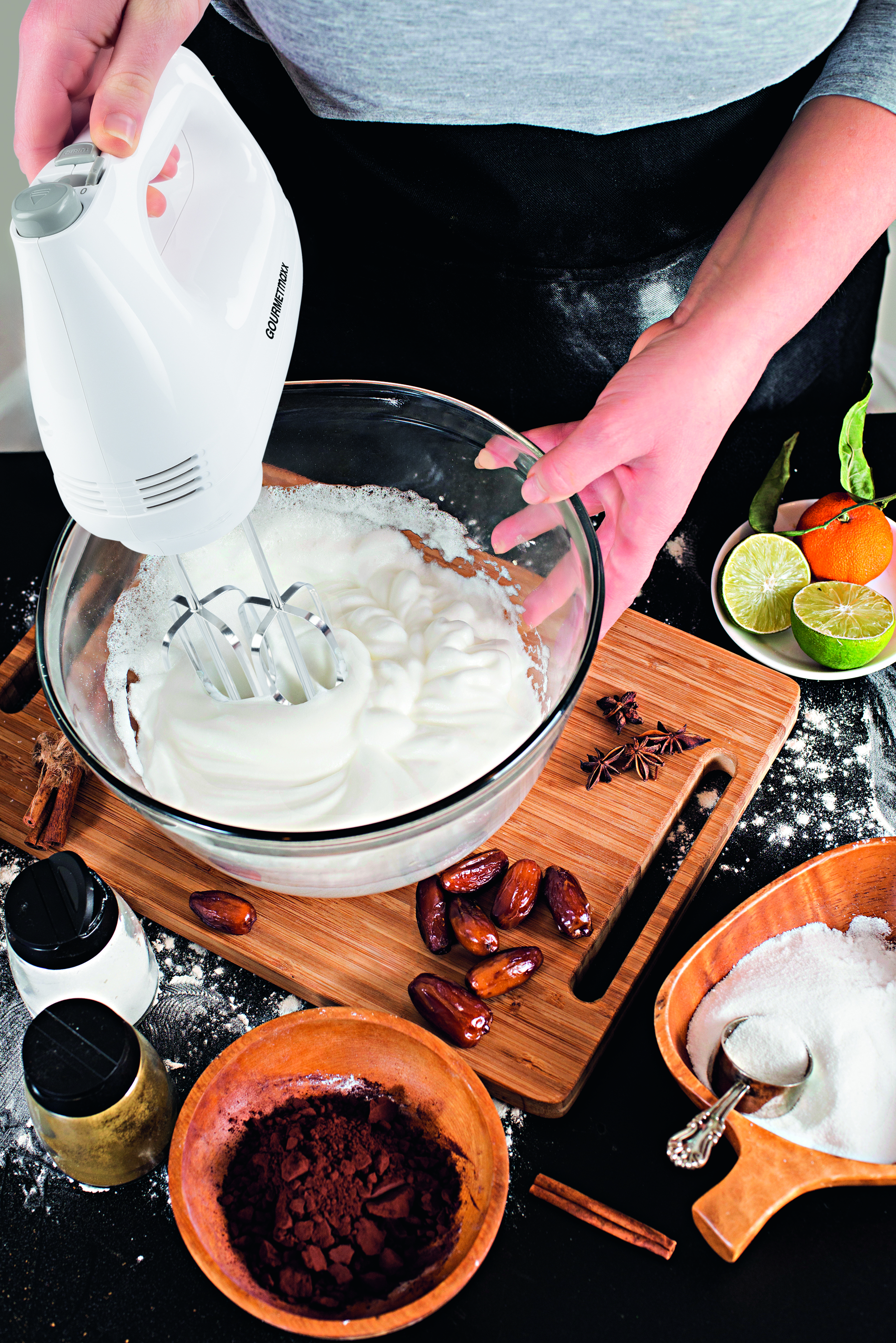 Eine Person schlägt Eier in einer Glasschüssel mit einem Handmixer auf. Zutaten wie Datteln und Kakaopulver liegen bereit.