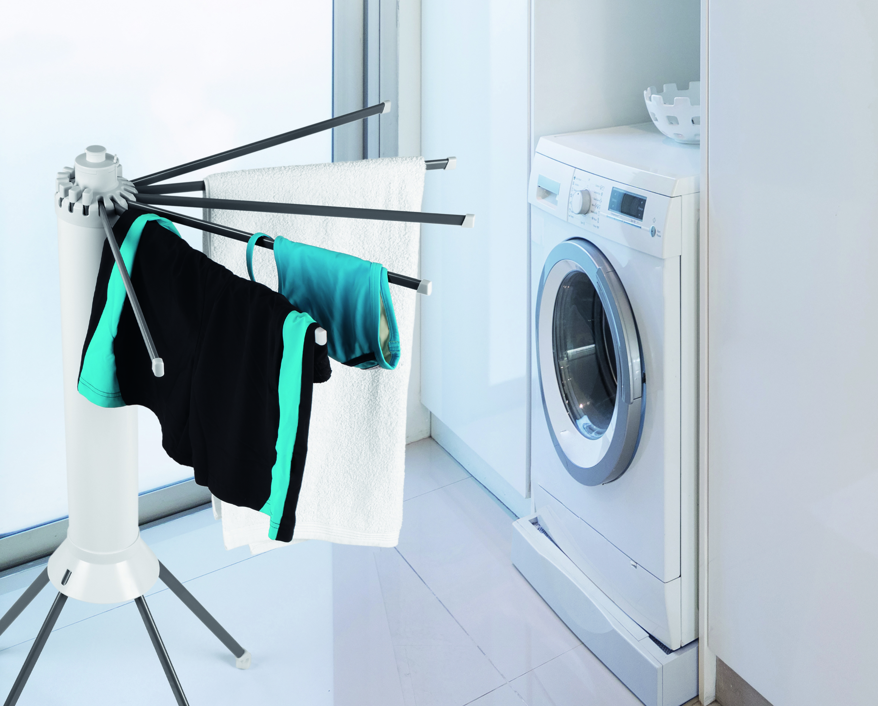 Ein Wäschetrockner mit Kleidung und Handtüchern. Eine Waschmaschine ist in der Nähe.