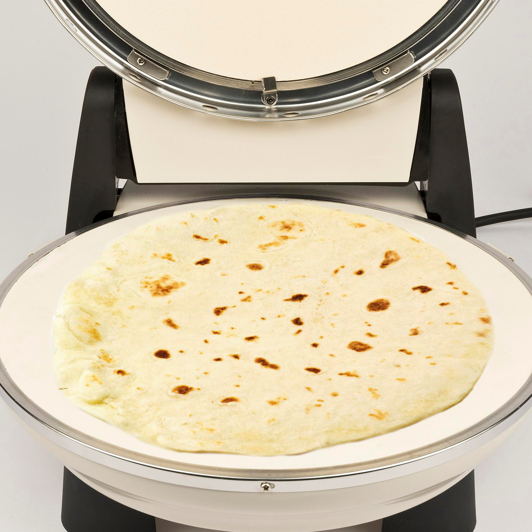 Eine Tortilla liegt auf einer weißen Grillplatte in einem geschlossenen Tortilla-Maker. Der Maker ist schwarz und weiß.