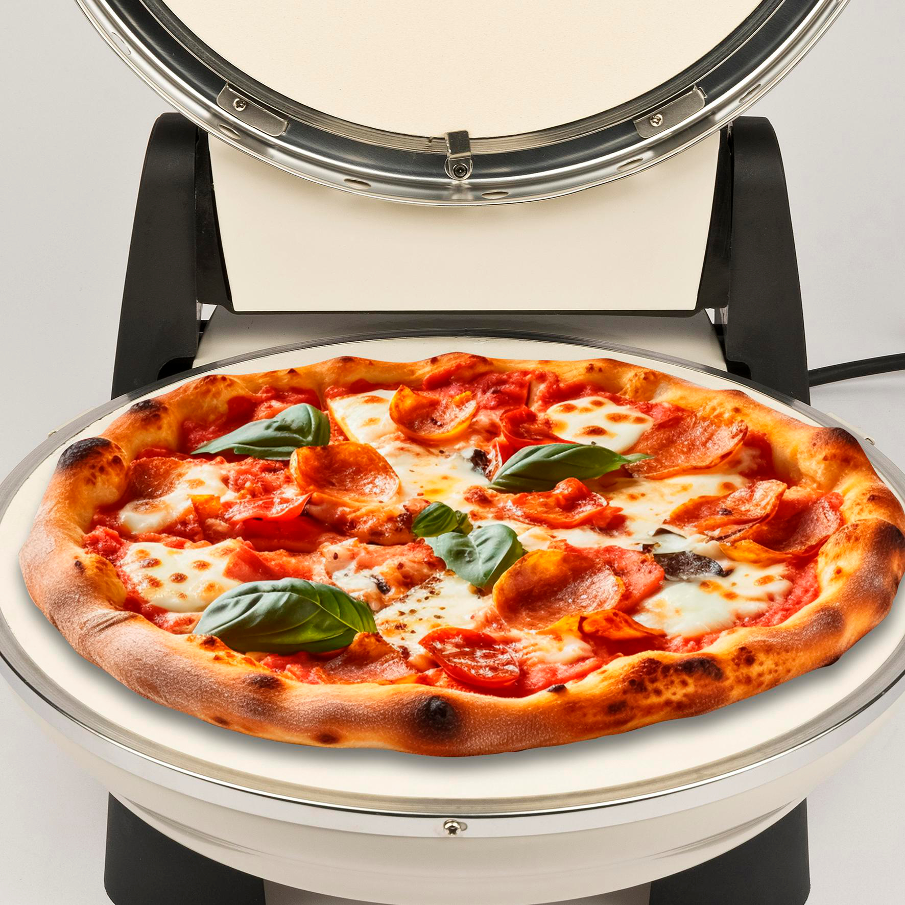 Eine Pizza mit Peperoni, Basilikum und Mozzarella liegt in einem Pizzaofen. Der Ofen ist offen, die Pizza liegt in der Mitte.