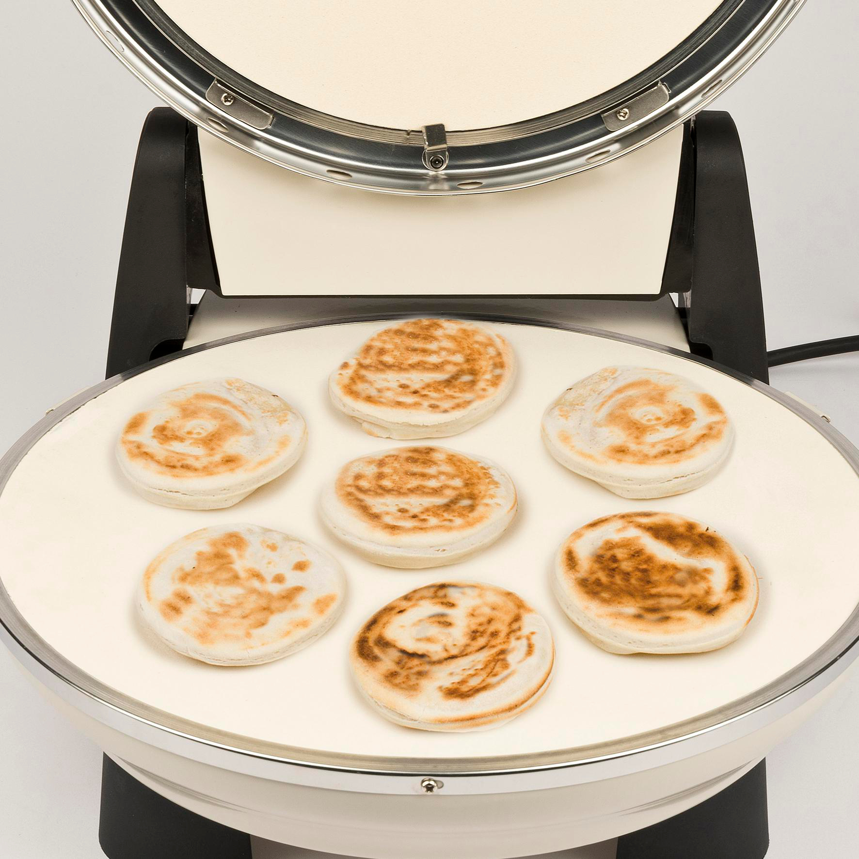Ein Pfannkuchenmacher mit sieben gekochten Pfannkuchen auf einer weißen Oberfläche. Der Maker ist weiß und silber, mit schwarzem Sockel.