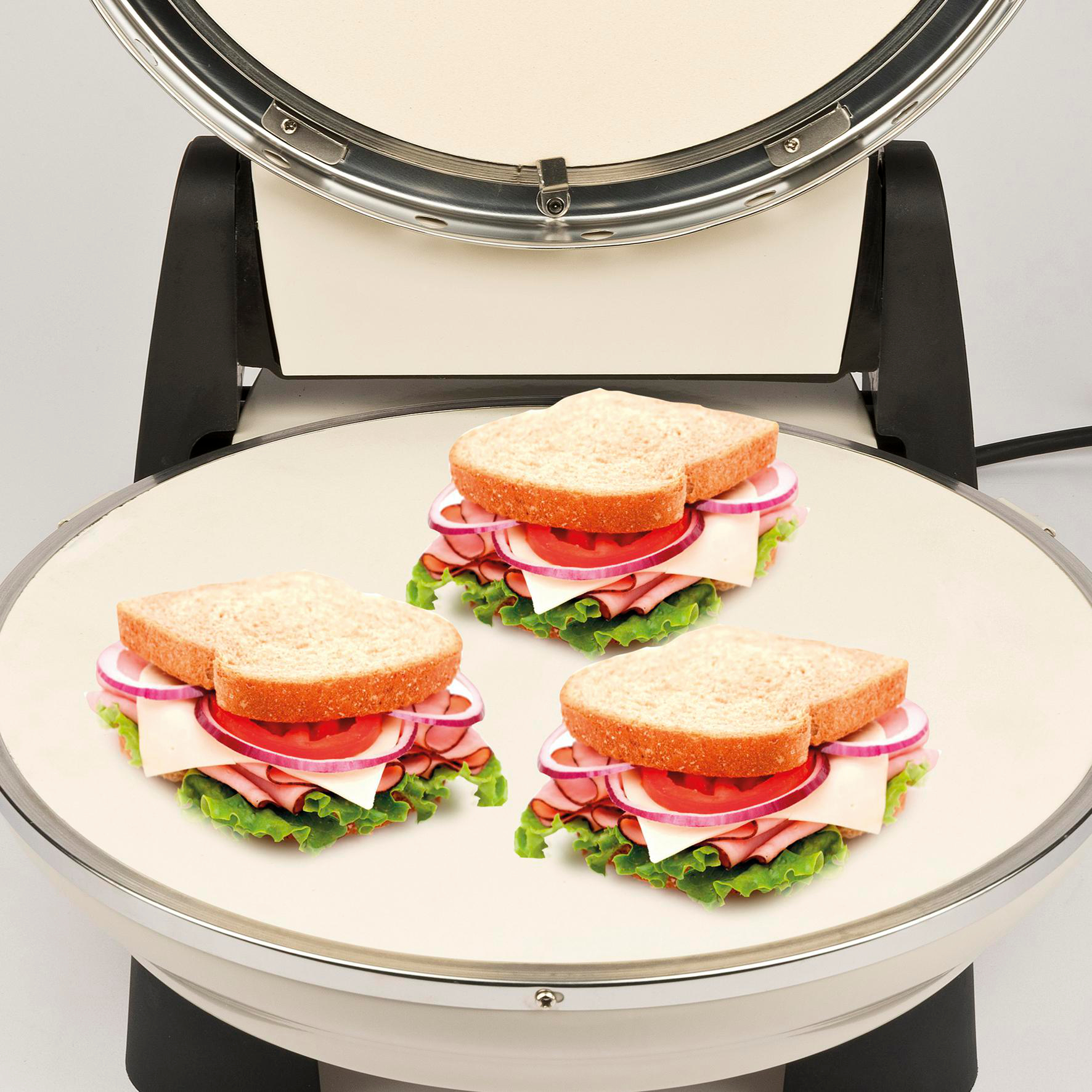 Drei Sandwiches mit Schinken, Käse, Tomaten und roten Zwiebeln liegen auf einer Grillplatte. Die Grillplatte ist Teil eines Sandwichmakers.