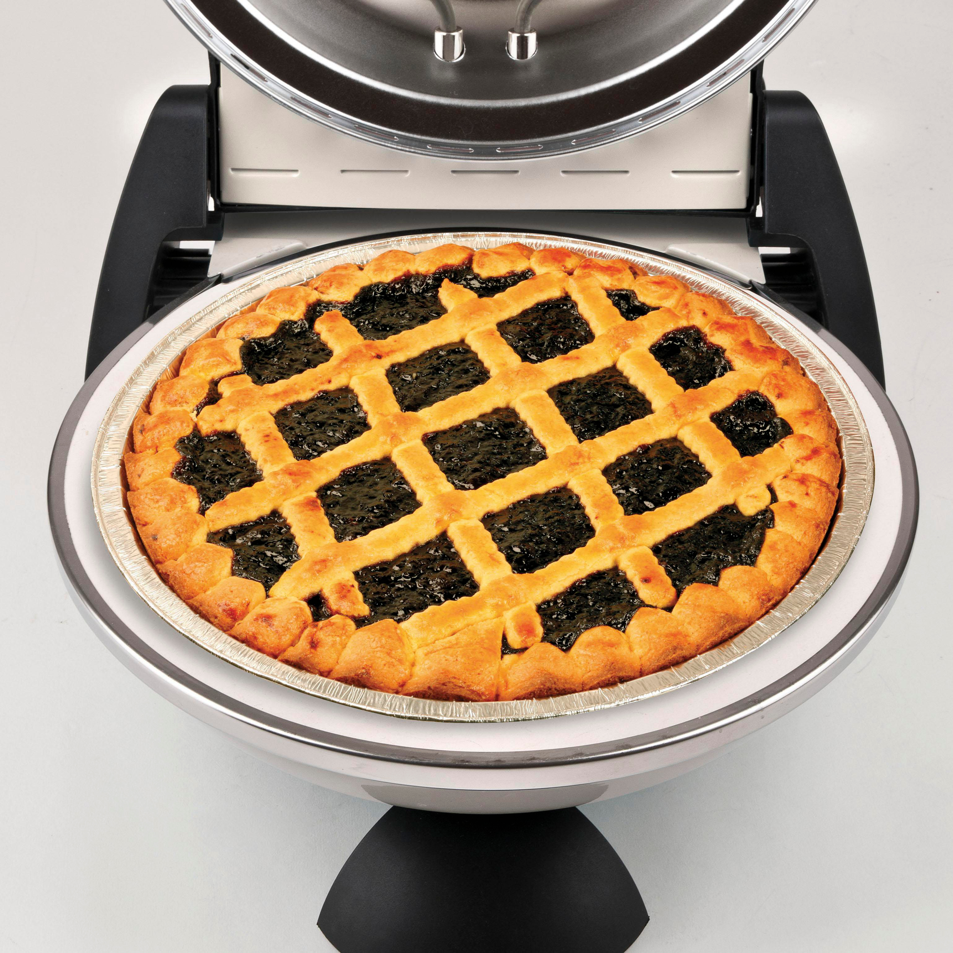 Ein gebackener Kuchen in einer Silberform liegt in einem Kuchenbereiter. Der Kuchen hat einen Gitterteig und dunkle Füllung.