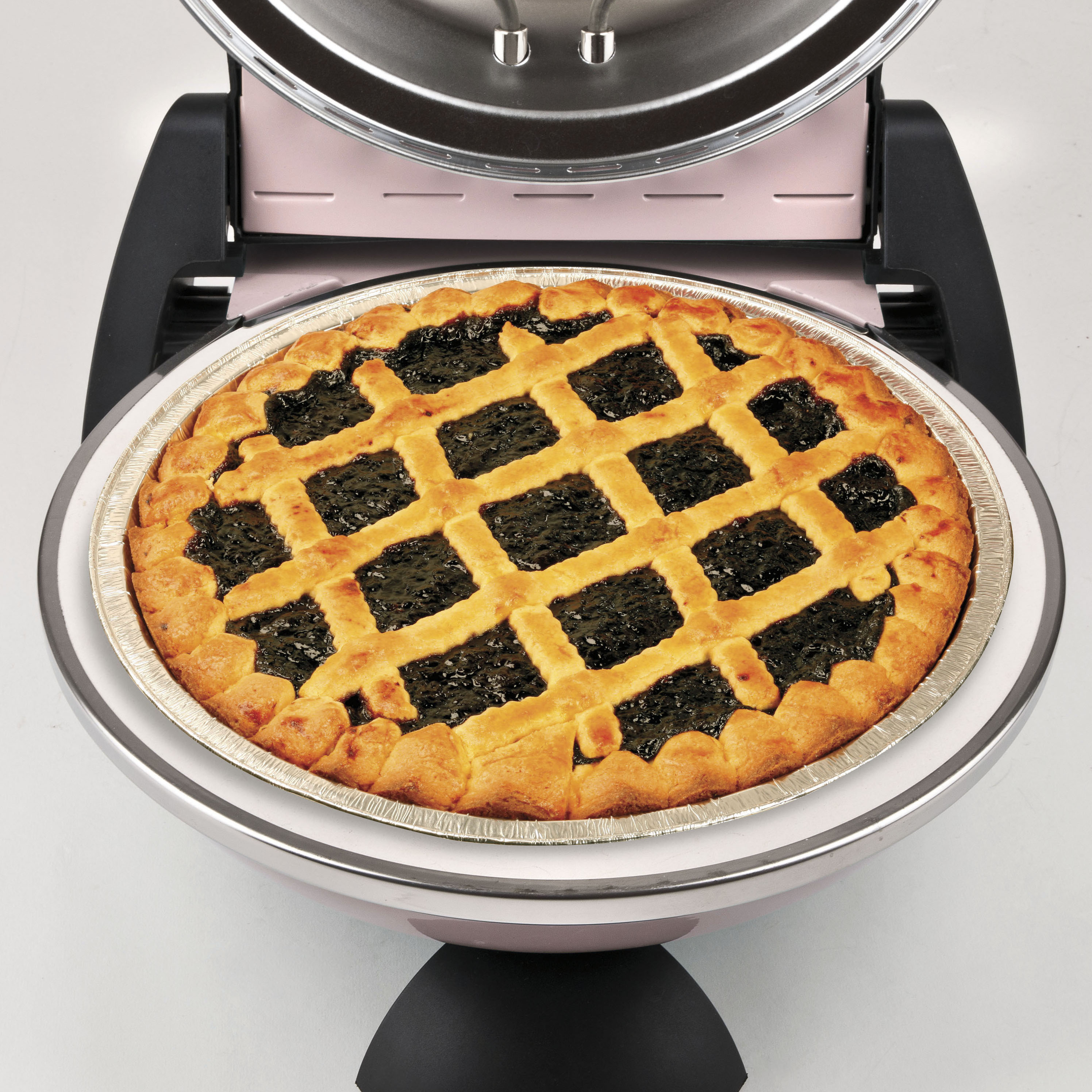 Nahaufnahme eines Kuchens in einem rosa Gerät. Der Kuchen hat einen Gitterteig und eine dunkle Füllung. Das Gerät ist offen.