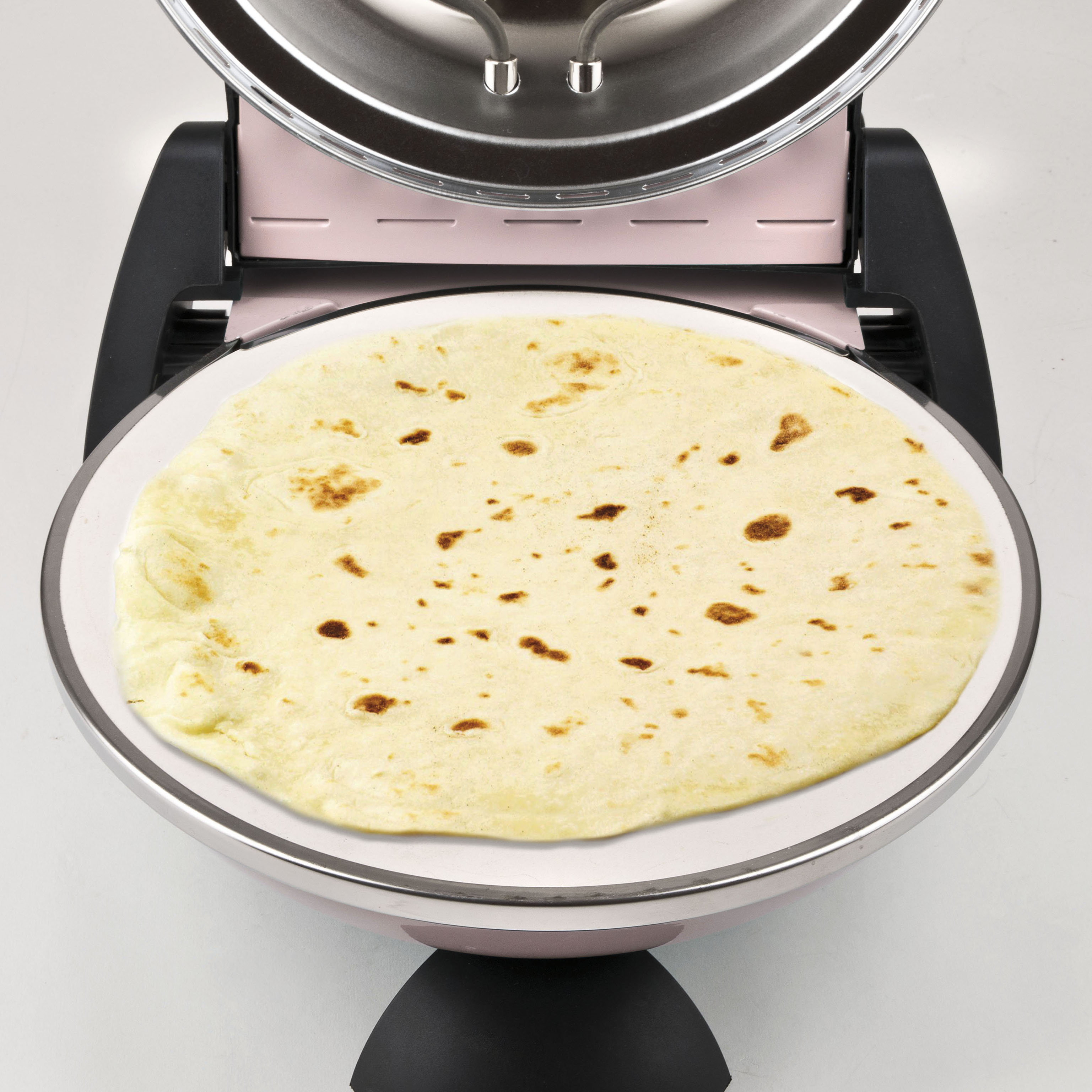 Eine Tortilla liegt auf einem rosa Elektrogrill. Die Tortilla ist hellbraun mit dunkleren braunen Flecken. Der Grill ist offen.