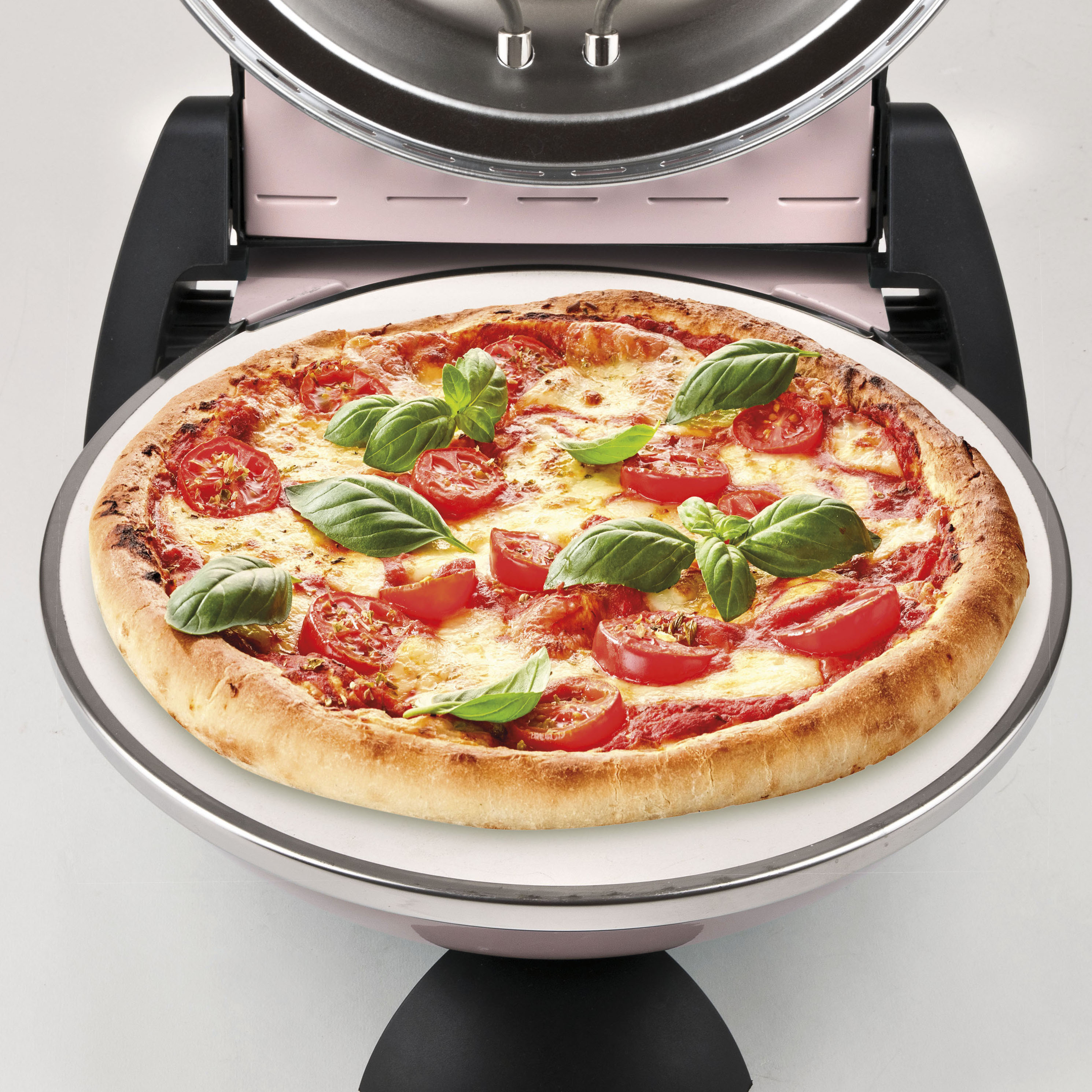 Eine Pizza mit Tomaten und Basilikum befindet sich in einem rosa Pizzaofen. Der Ofen ist offen und zeigt Heizelemente.