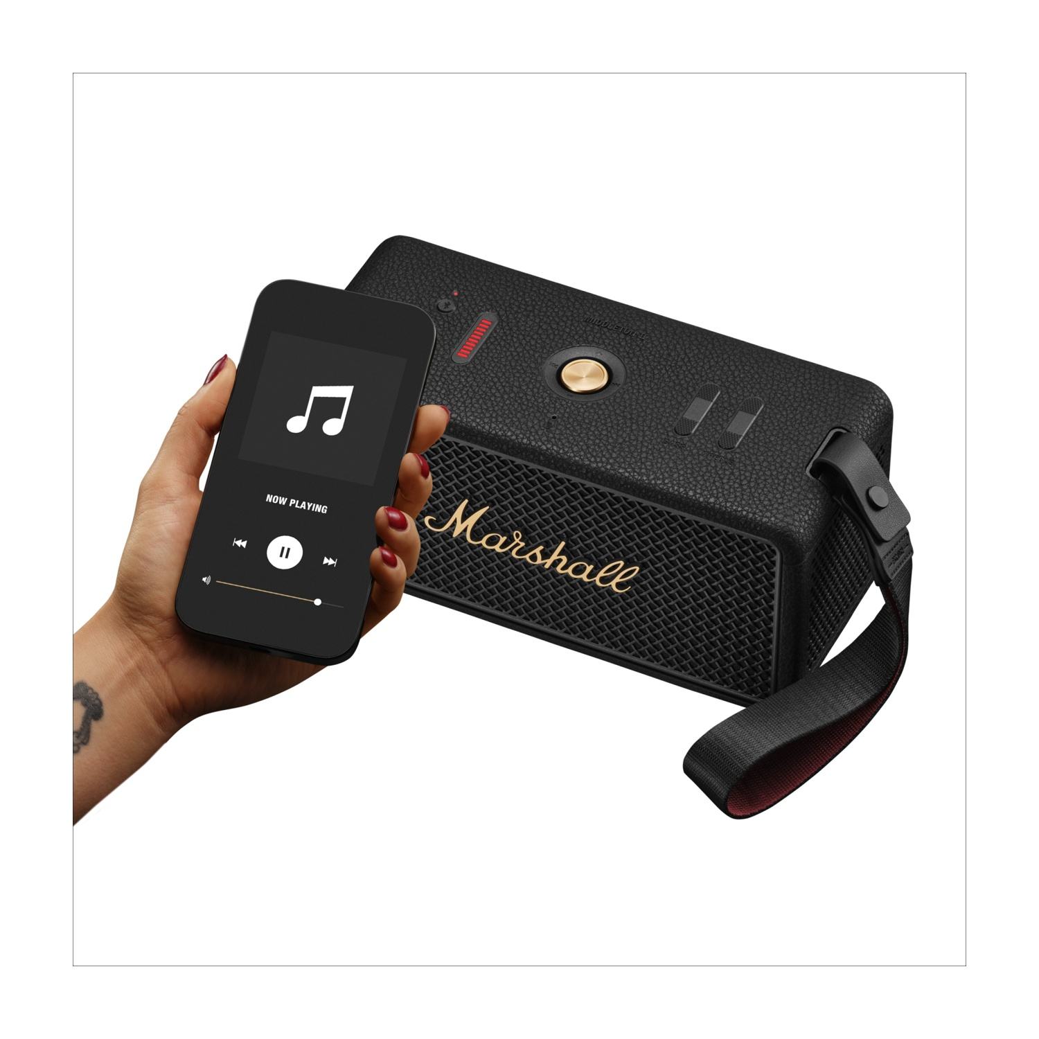Una mano tiene in mano un telefono nero che mostra i controlli musicali. Accanto c'è un altoparlante Marshall nero con logo dorato.