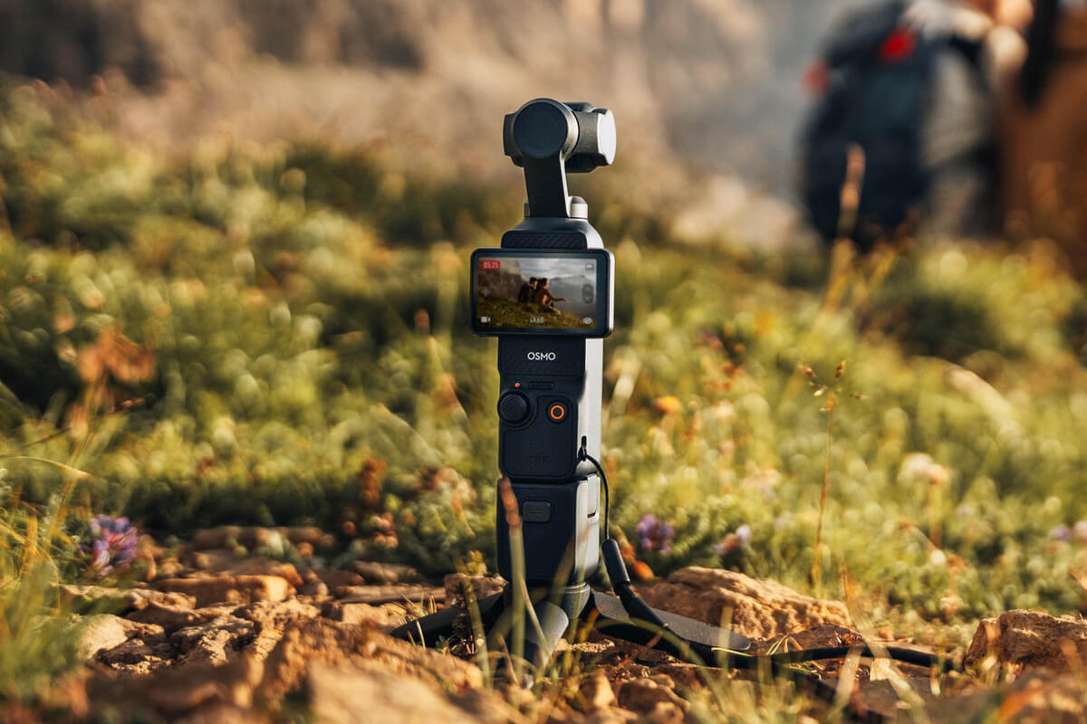 Bir tripod üzerindeki siyah bir Osmo kamera, bir video gösteriyor. Bir kişi arka planda bulanık.