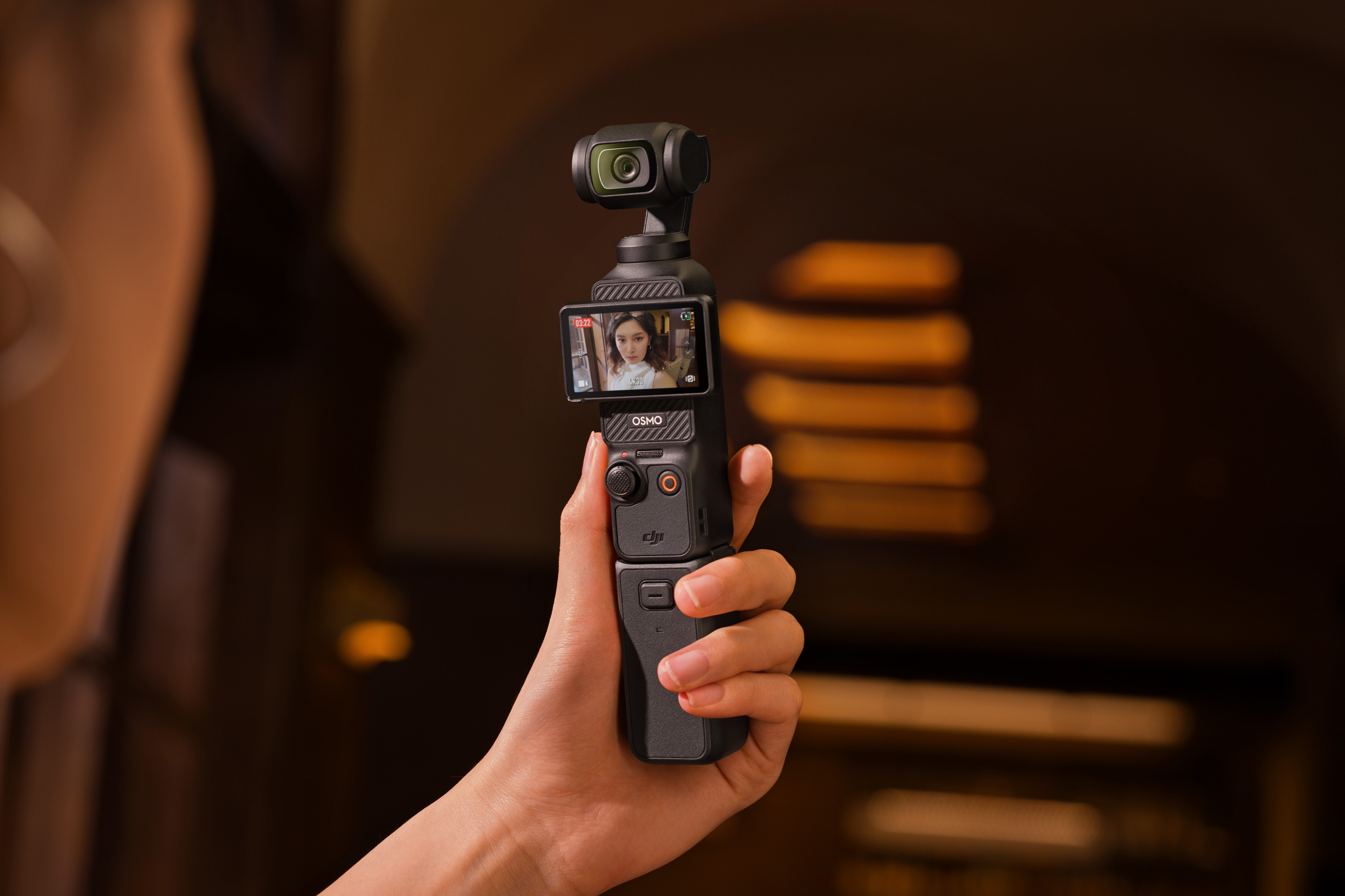 Bir el, ekranda bir kadın gösteren siyah bir Osmo Pocket kamerayı tutuyor. Kahverengi arka plan.