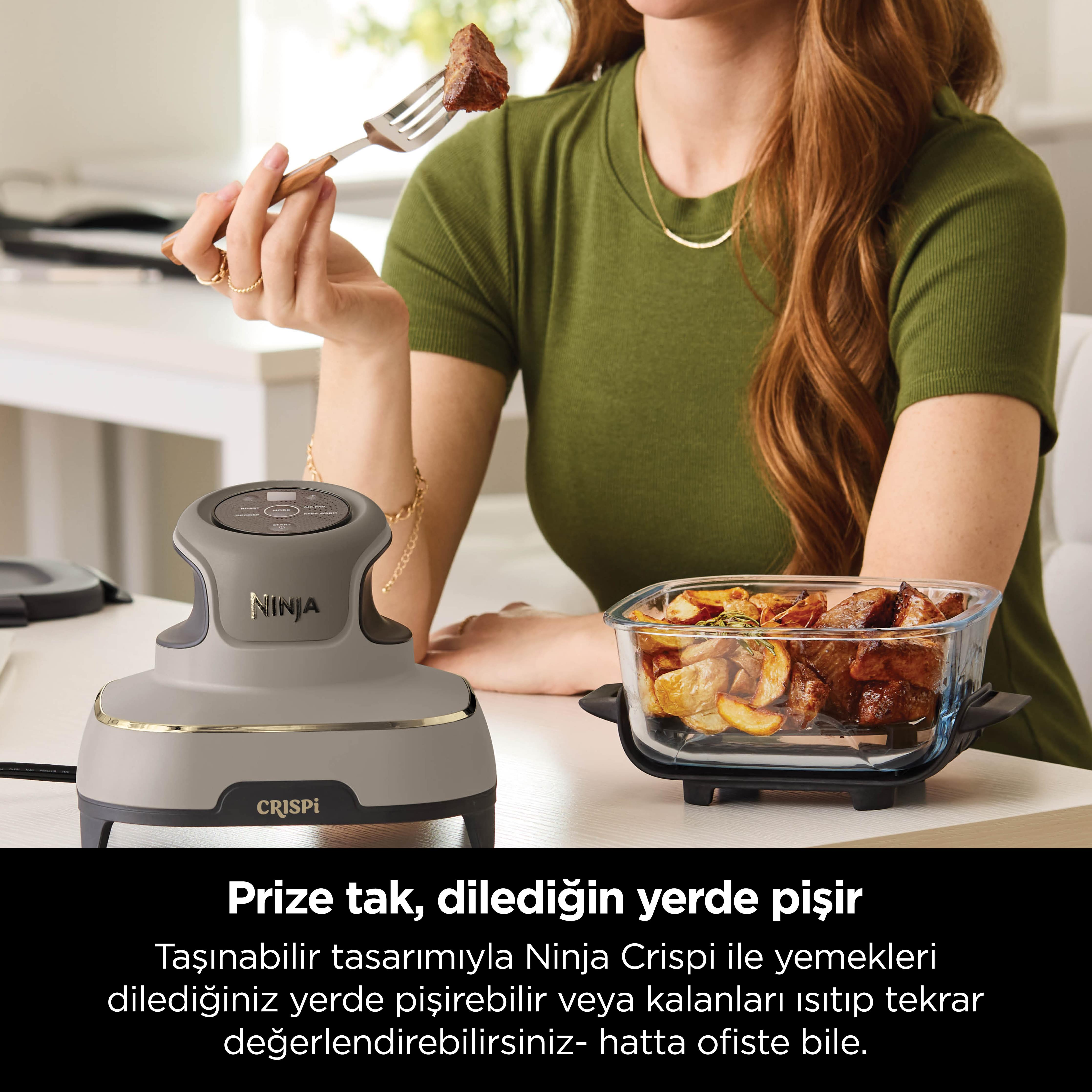 Bir kadın bir masanın üzerinde yemek dolu bir çatal tutuyor. Masada bir Ninja Crispi fritözü ve yiyecekler var.
