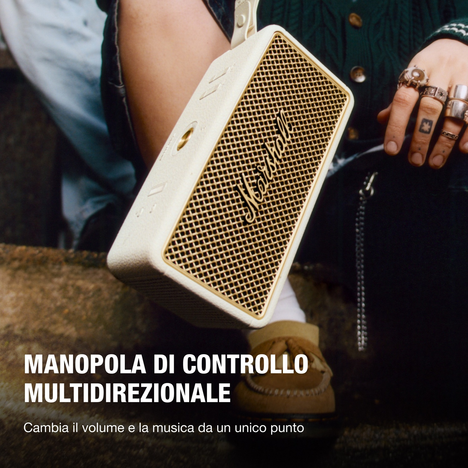 Una persona tiene in mano un altoparlante Marshall color crema. La persona indossa anelli e un maglione verde. Il testo recita 'Manopola di controllo multidirezionale'.
